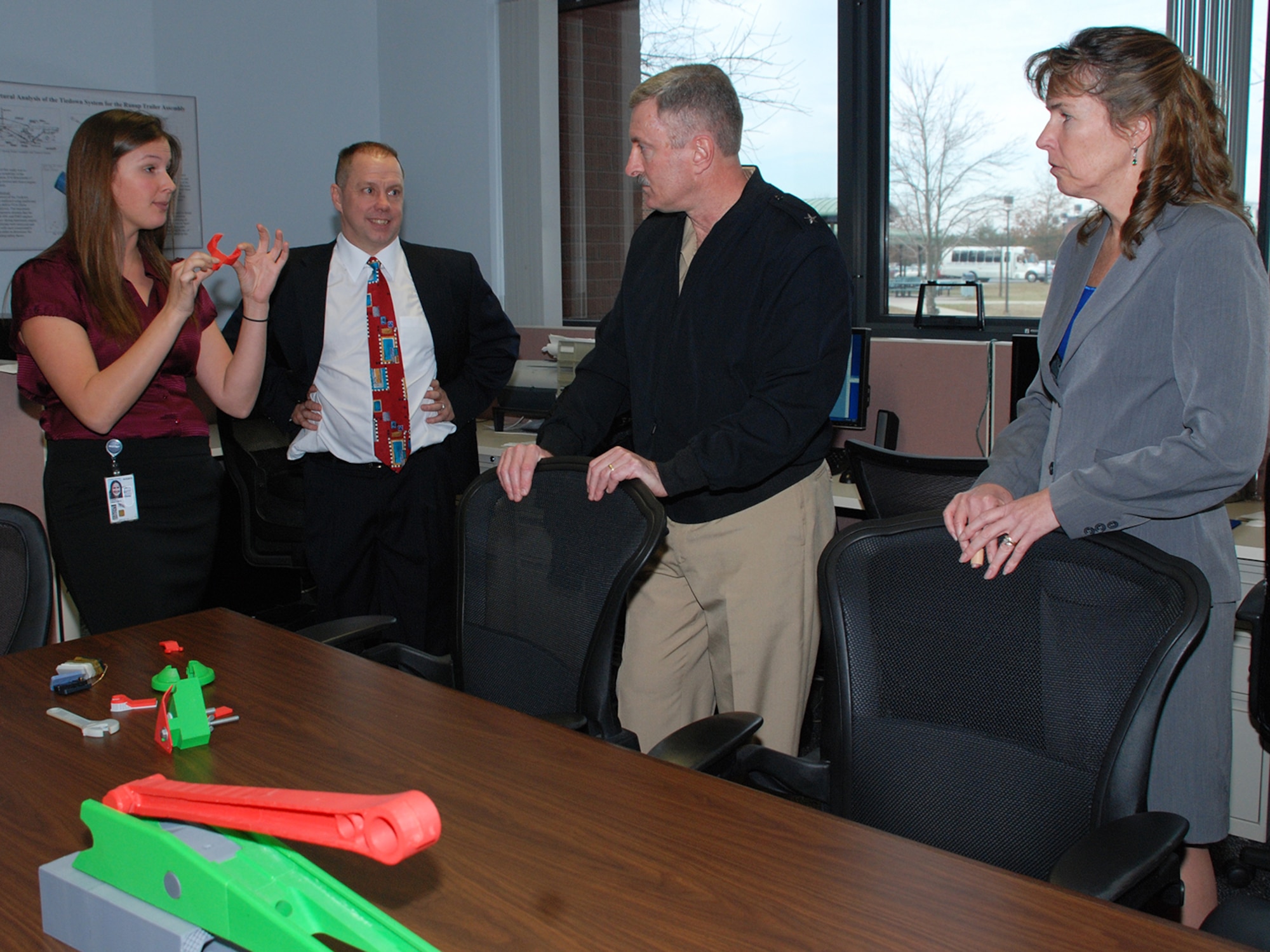 Mechanical engineer Christine Farrell describes the three-dimensional printing and rapid prototyping capabilities of Lakehurst’s Support Equipment Division to Rear Adm. Mark Darrah during his visit Jan. 9, 2013, to Joint Base McGuire-Dix-Lakehurst, N.J.  Farrell is holding a 3D printed model of the MH-60R Oil Line Nut Wrench that saves 80 man hours per routine helicopter oil change.  The models are used for fit and function testing, as well as early problem detection.  Looking on are John Schmelzle and Kathleen Donnelly. (U.S. Navy courtesy photo/Released)