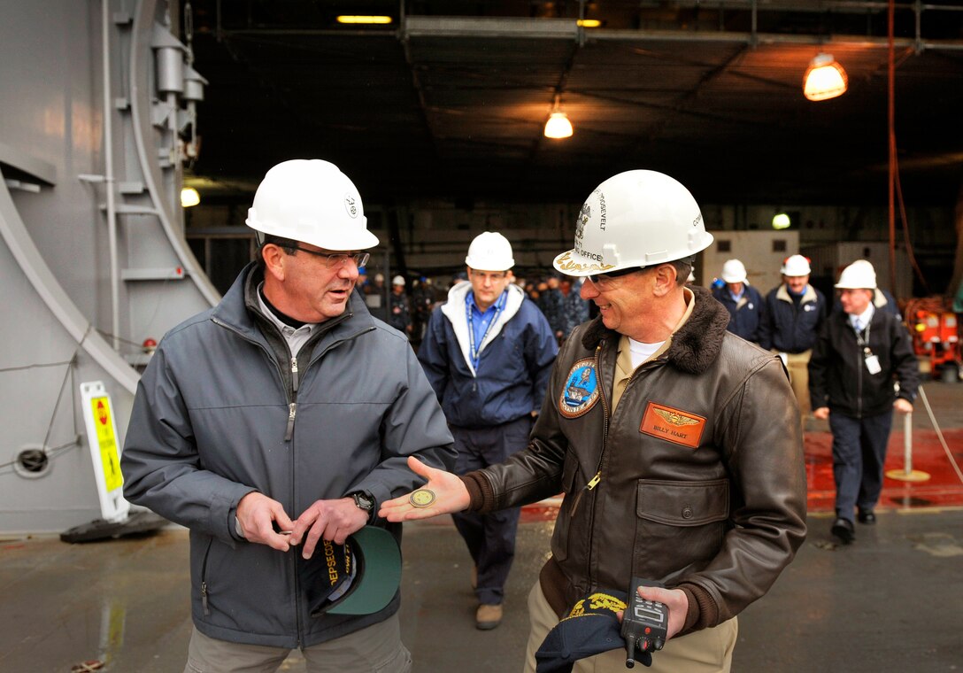 Navy Capt. William J. Hart, right, commanding officer of the aircraft carrier USS Theodore Roosevelt, offers Deputy Defense Secretary Ashton B. Carter, left, the ship's coin after he visited sailors and shipyard workers in Norfolk, Va., Jan. 17, 2013.