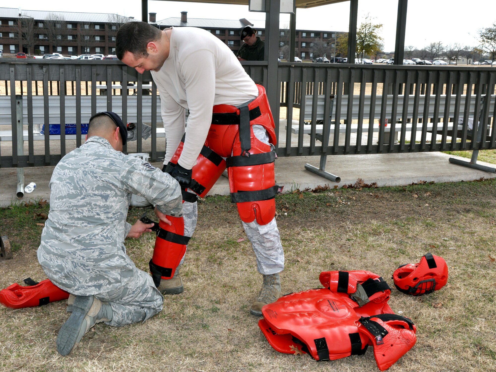 GOODFELLOW AIR FORCE BASE, Texas--  Staff Sgt. Luis Alcantar, 17th Security Forces Squadron training NCO-in-charge, helps Capt. Chris Heinen, SFS operations officer, into the red mad suite, Jan. 15, outside the SFS building. The heavily padded suite provides protection while the Airmen in training fight him using a training extendable baton, one of three weapons highlighted in the SFS non-lethal weapons training. (U.S. Air Force photo/Airman 1st Class Jessica Keith)