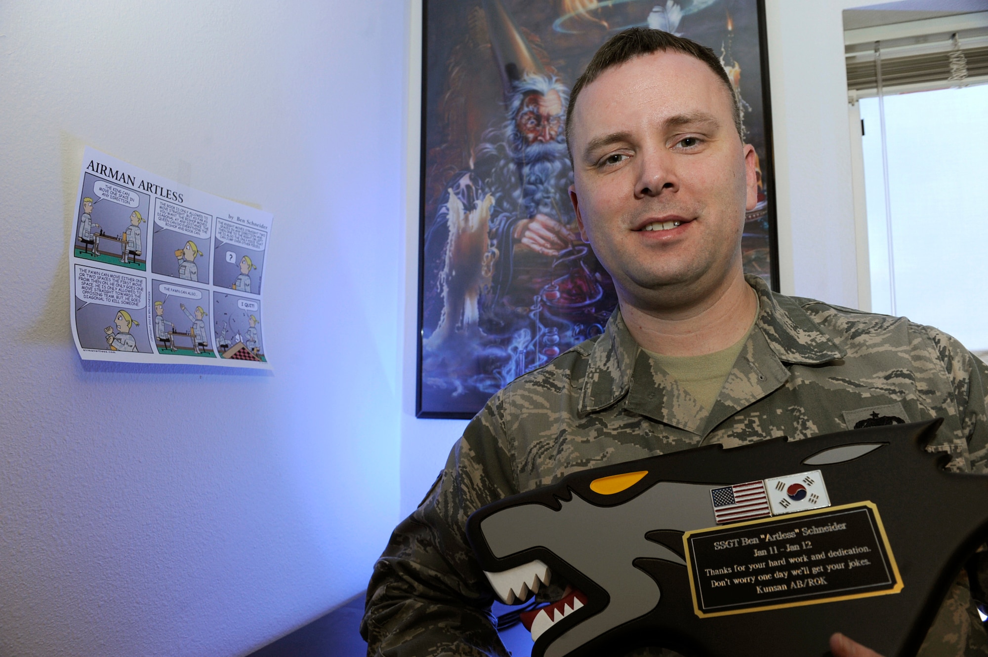 Air Force Staff Sgt. Benjamin Schneider shows off the plaque recognizing his cartoon work, received from his assignment in Korea, in his home office on JBER Jan.14. Schneider is a cartoonist, creating the comical graphics as a hobby. His work has been published in the Okahoma Daily, the Aviano Air Base's the Vigileer in Italy, Kadena Air Base's Samurai Gate in Japan, U.S. Air Foces in Europe's Air Scoop Magazine, and the bi-weekly Crimson Sky in Korea. His work is also available on his website http://airmanartless.com. He is a training monitor for the 3rd Munitions Squadron. His hometown is Newscastle, Okla. (U.S. Air Force photo/Staff Sgt. Robert Barnett)