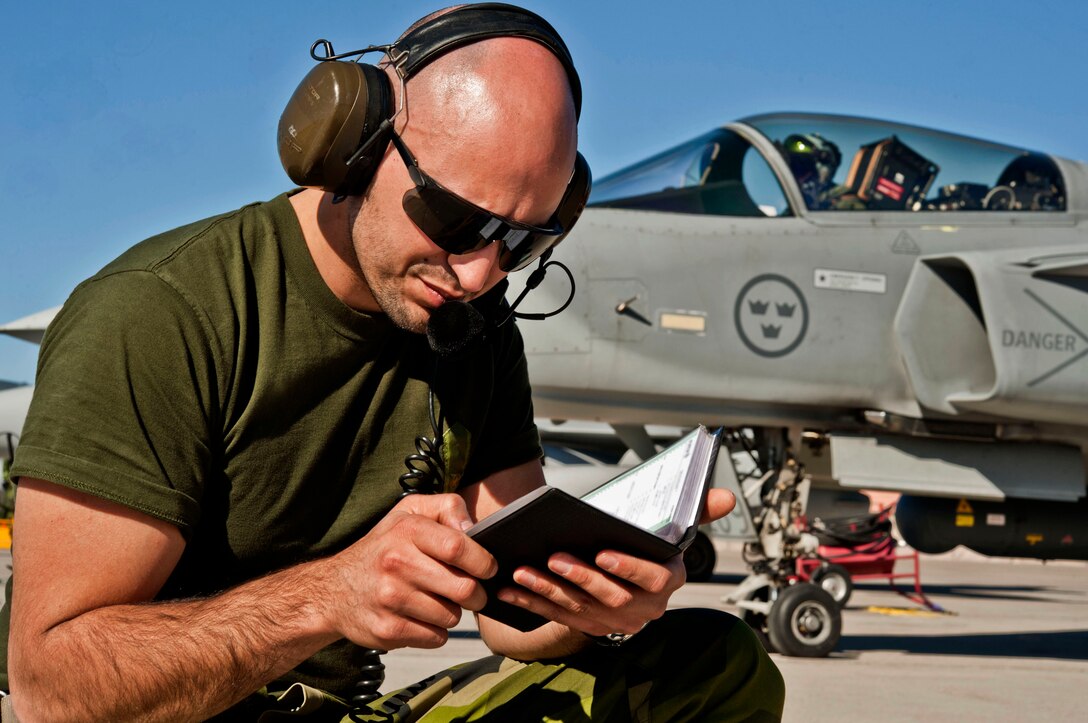 A Swedish crew chief looks at an aircraft manual before launching a Swedish JAS-39 Gripen fighter jet during exercise Red-Flag 13-2 on Nellis Air Force Base, Nev., Jan. 21, 2013. The crew chief is assigned to the 172nd Fighter Reconnaissance Squadron.