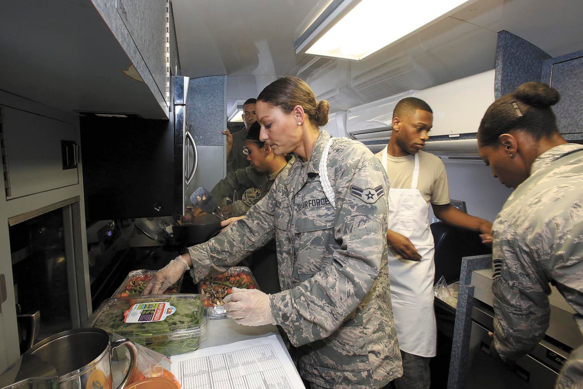 Airman 1st Class Christina Hall (center), and Staff Sgts. Demarious Beard and Sheila Fitzgerald prepare the dinner portion of a three-course gourmet meal for Gen. Edward A. Rice, his wife Teresa and staffers aboard the Boeing KC135 trainer aircraft, nicknamed "Speckled Trout." These student flight attendants are practicing their service techniques as part of a flight attendant class at JBSA-Lackland. (Photo by Robbin Cresswell)