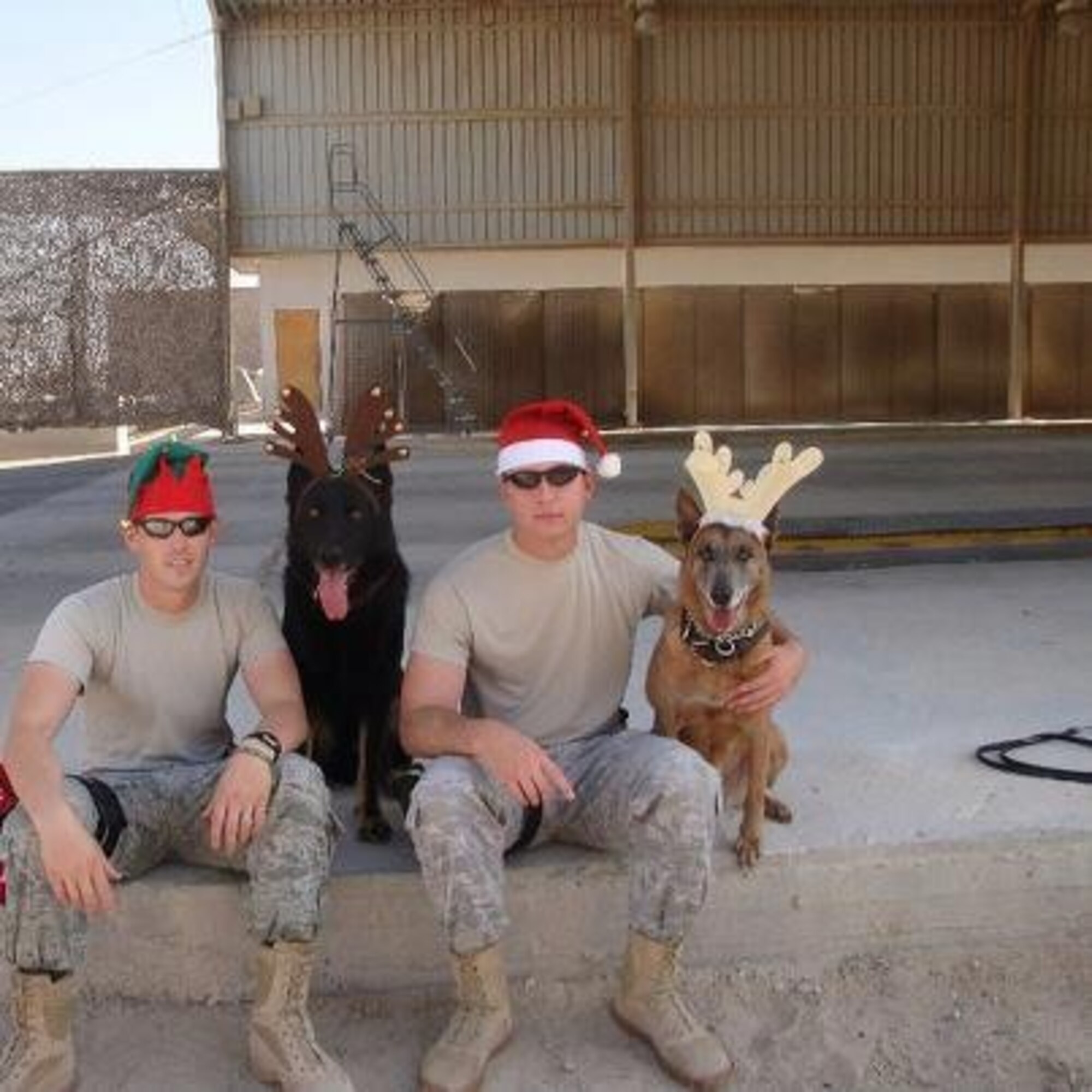 From left, U.S. Staff Sgt. James Colip, 366th Security Forces Squadron military working dog handler and his dog Cezar sit with U.S. Air Force Staff Sgt. Robert Wilson, 366th SFS military working dog handler and his dog Tanja, pose for a photo outside the search pit at an undisclosed location in southwest Asia in December 2010. Wilson and Tanja were partnered together for 19 months. (Courtesy photo)