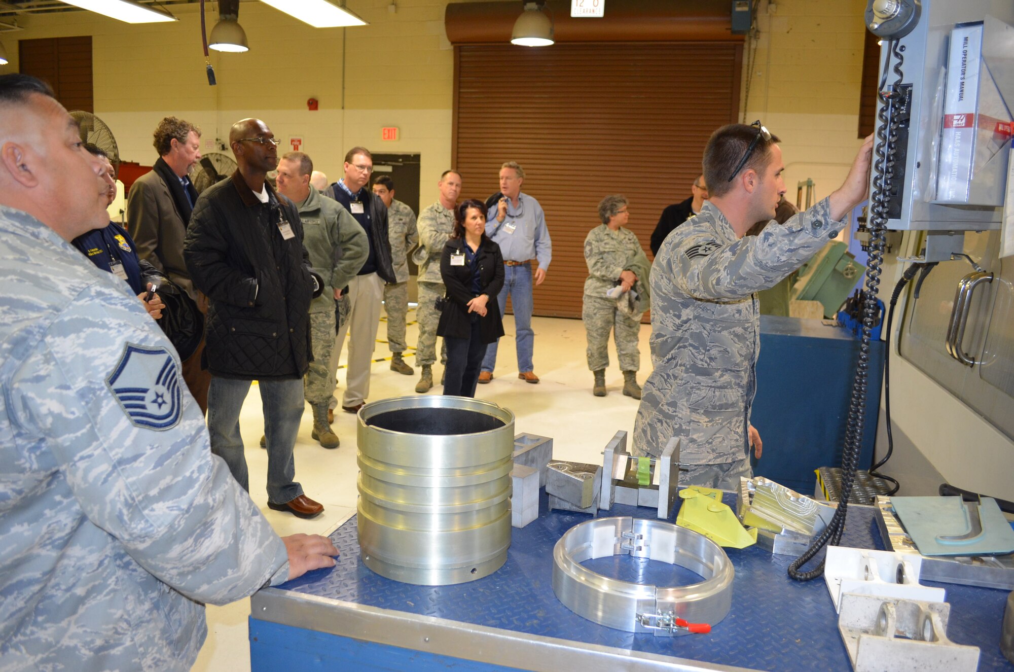 Staff Sgt. Steve Morris a metals technician, with the 433rd Metals Technology shop, demonstrates the computer numerical control mill center, while Master Sgt. Fidencio "Pete" Ramon the metals’ shop chief looks on. The demonstration was performed for 15 visiting Honorary Commanders of the 433rd Airlift Wing, who visited the wing on Jan. 18, 2013 for a tour of the wing's maintenance mission. The Honorary Commander program assigns area civic and business leaders to wing senior leadership to educate them about the wing's mission and the role they play with the Reserve forces and National Defense. (U.S. Air Force Photo/Major Timothy Wade)
