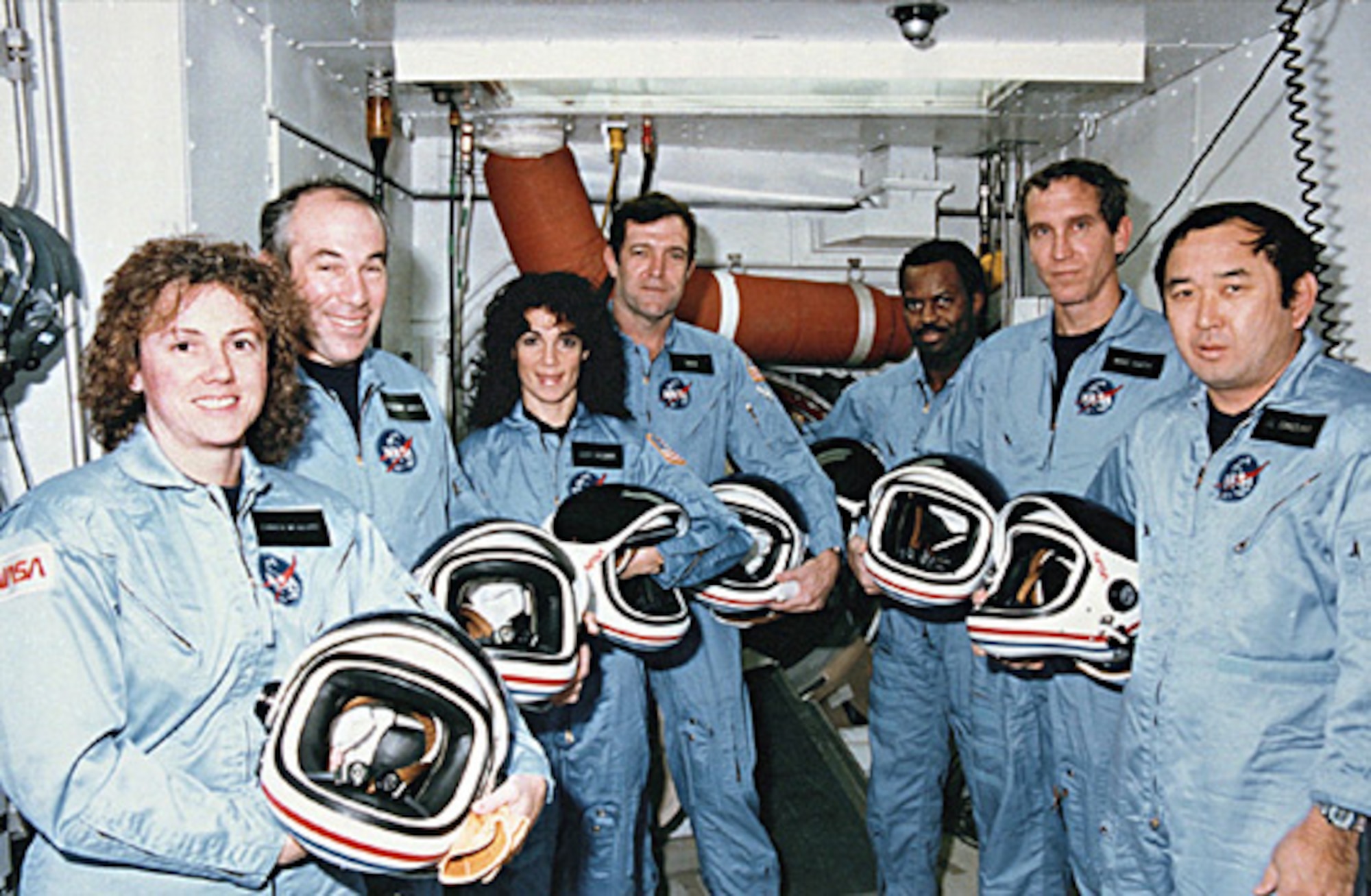 The Challenger crew outside the shuttle's hatch on a prelaunch visit. From left: Christa McAuliffe, Gregory Jarvis, Judith Resnick, Francis (Dick) Scobee, Ron McNair, Michael Smith, and Ellison Onizuka. (Photo courtesy of NASA/Released)