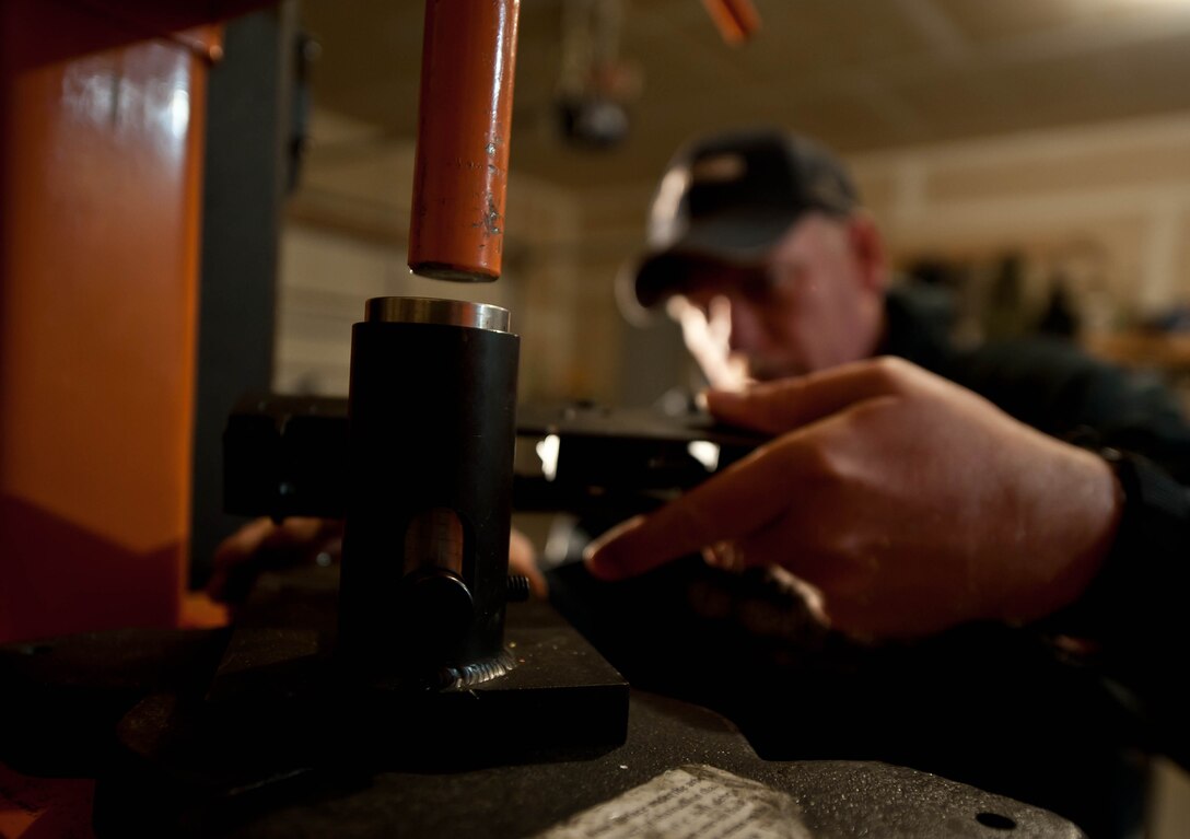 Master Sgt. Monte Ealy, 28th Civil Engineer readiness and emergency management NCO in charge, uses a 12-ton shop press to forge the body frame of a custom made AK- pattern semi-automatic rifle replica in Rapid City, S.D., Dec. 11, 2012. Ealy says that rifle building is an art that requires a good amount of ingenuity, a drill press, a 12-ton shop press, and a variety of other tools required by craftsmen gunsmiths. (U.S. Air Force photo by Airman 1st Class Zachary Hada/Released)