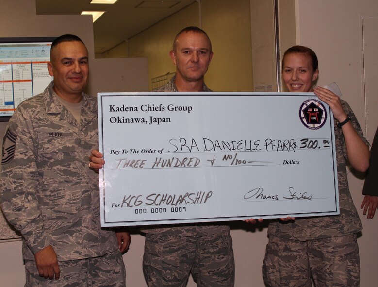 U.S. Air Force Chief Master Sgt. Ronnie Brady, Kadena Chiefs Group treasurer, and Chief Master Sgt. Ted Plaza, Scholarship Selection Committee lead, award Senior Airman Danielle Pfarr, 961st Airborne Air Control Squadron air surveillance technician, a $300 check for her essay on “Should Air Force enlisted members have advanced degrees?” Her essay succinctly presented the responsibility and opportunity Airmen have in obtaining advanced degrees that develop their critical thinking and problem solving skills essential to creating talented leaders for the Air Force. (U.S. Air Force courtesy photo)