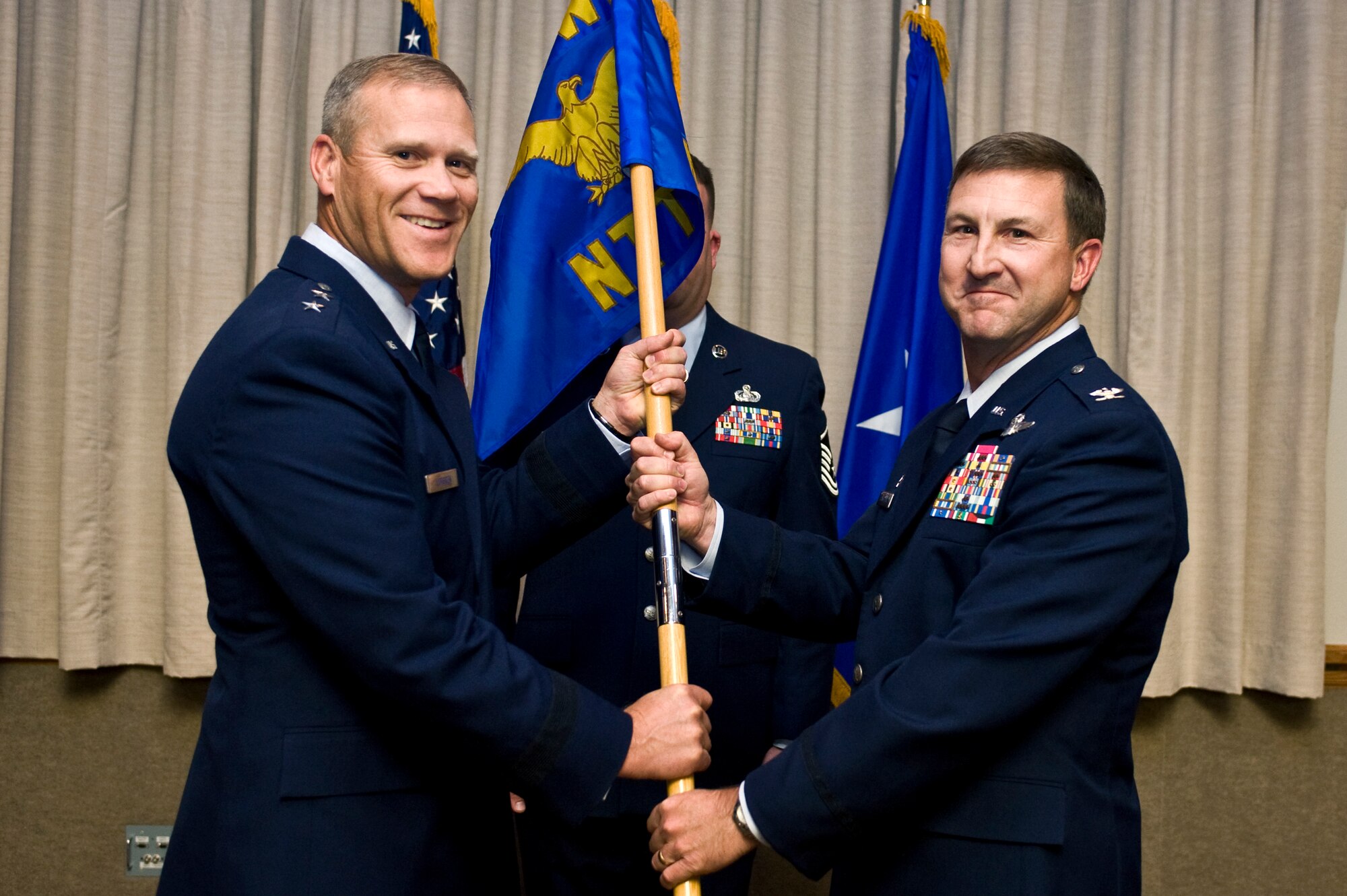 Maj. Gen. Jeffrey Lofgren, U.S. Air Force Warfare Center commander, passes the Nevada Test and Training Range flag to Col. Stephen Langford, NTTR commander, during the NTTR assumption of command ceremony, Jan. 28, 2013, at Nellis Air Force Base, Nev. The NTTR, formerly the 98th Range Wing, provides the warfighter a flexible, realistic and multidimensional battle-space to conduct testing, training and tactics development in support of U.S. national interests. (U.S. Air Force photo by Senior Airman Matthew Lancaster)