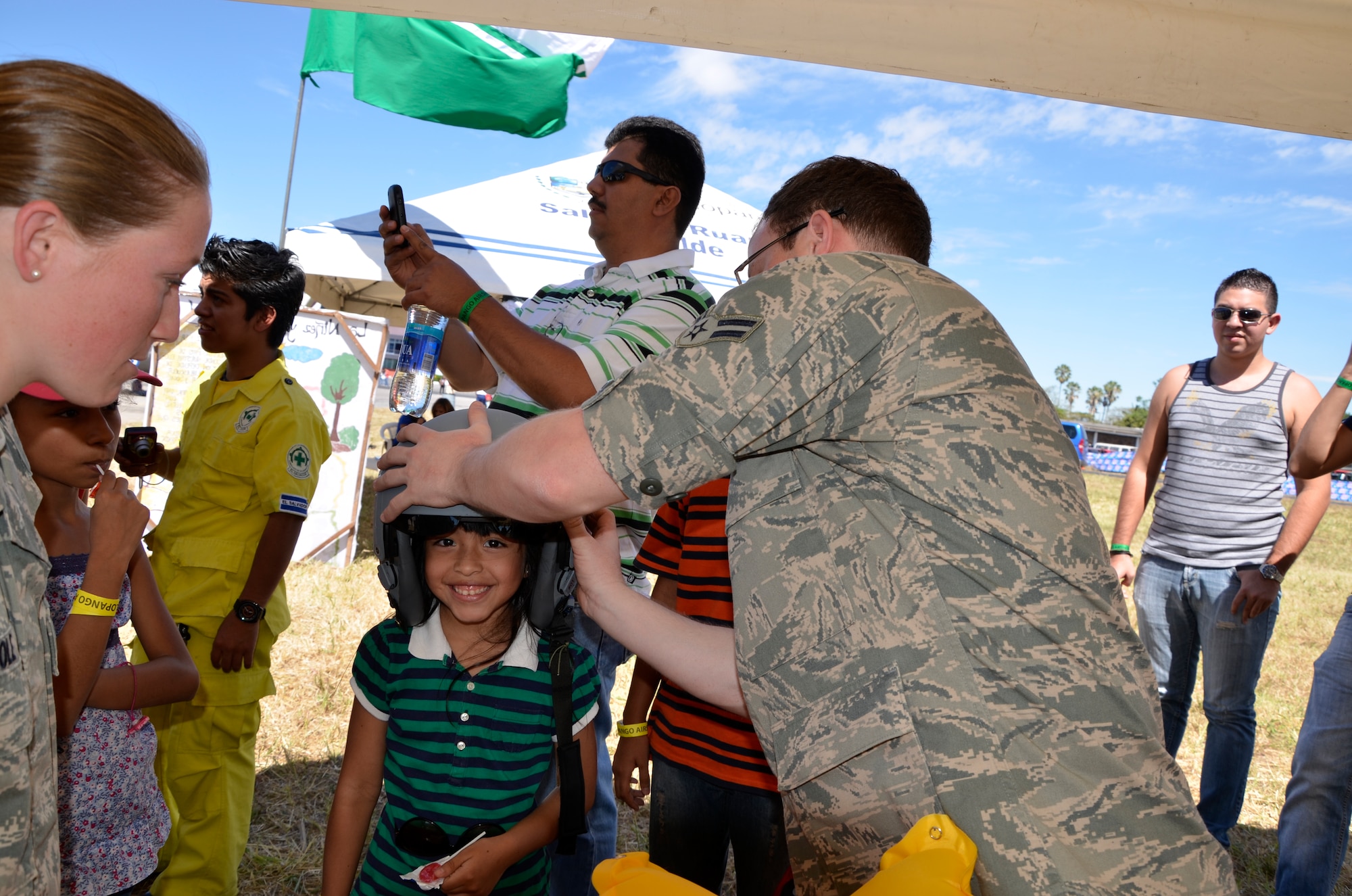 U.S. Air Force Airman 1st Class Alex Allbee assists a Salvadoran child wearing an aircrew flight helmet while Senior Airman Beverly Cole (left) translates information and instructions from English to Spanish at the 2013 Ilopango Air Show in Ilopango, El Salvador as part of a community relations event for the State Partnership Program January 26, 2013.  (N.H. National Guard photo by 1st Lt. Aaron McCarthy/RELEASED)