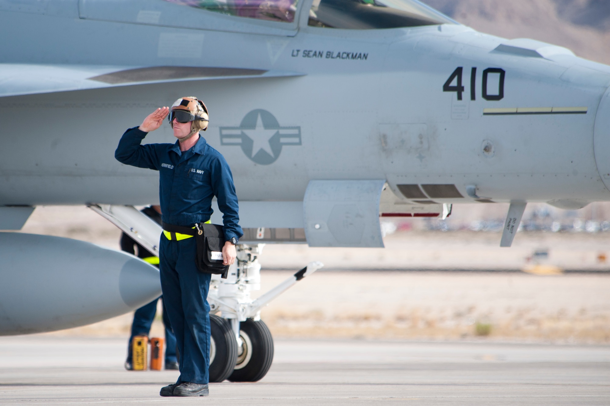 U.S. Navy Airman Ryan Merrifield, Strike Fighter Squadron 25 (VFA-25), Naval Air Station, Lemoore, Calif., plane captain, salutes as a signal of passing off ground control of an F/A-18E Hornet pilot prior to the aircraft taxiing onto the Nellis Air Force Base, Nev. active runway Jan. 25, 2013. The VFA-25 participation in Red Flag 13-2 trains ground workers on skills to launch aircraft in a joint and allied air forces training environment. (U.S. Air Force photo by Lawrence Crespo)
