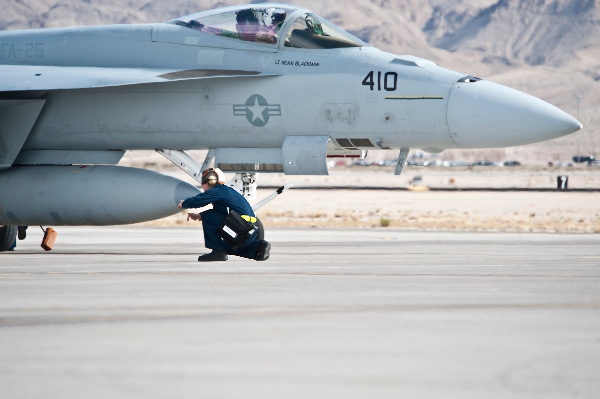 U.S. Navy Airman Ryan Merrifield, Strike Fighter Squadron 25 (VFA-25), Naval Air Station, Lemoore, Calif., plane captain, signals all clear below the F/A-18E Hornet prior to the aircraft taxiing onto the Nellis Air Force Base, Nev. active runway Jan. 25, 2013. The U.S. Navy’s participation in Red Flag 13-2 is to maximize their air combat readiness in a joint air-to-air training environment. (U.S. Air Force photo by Lawrence Crespo)