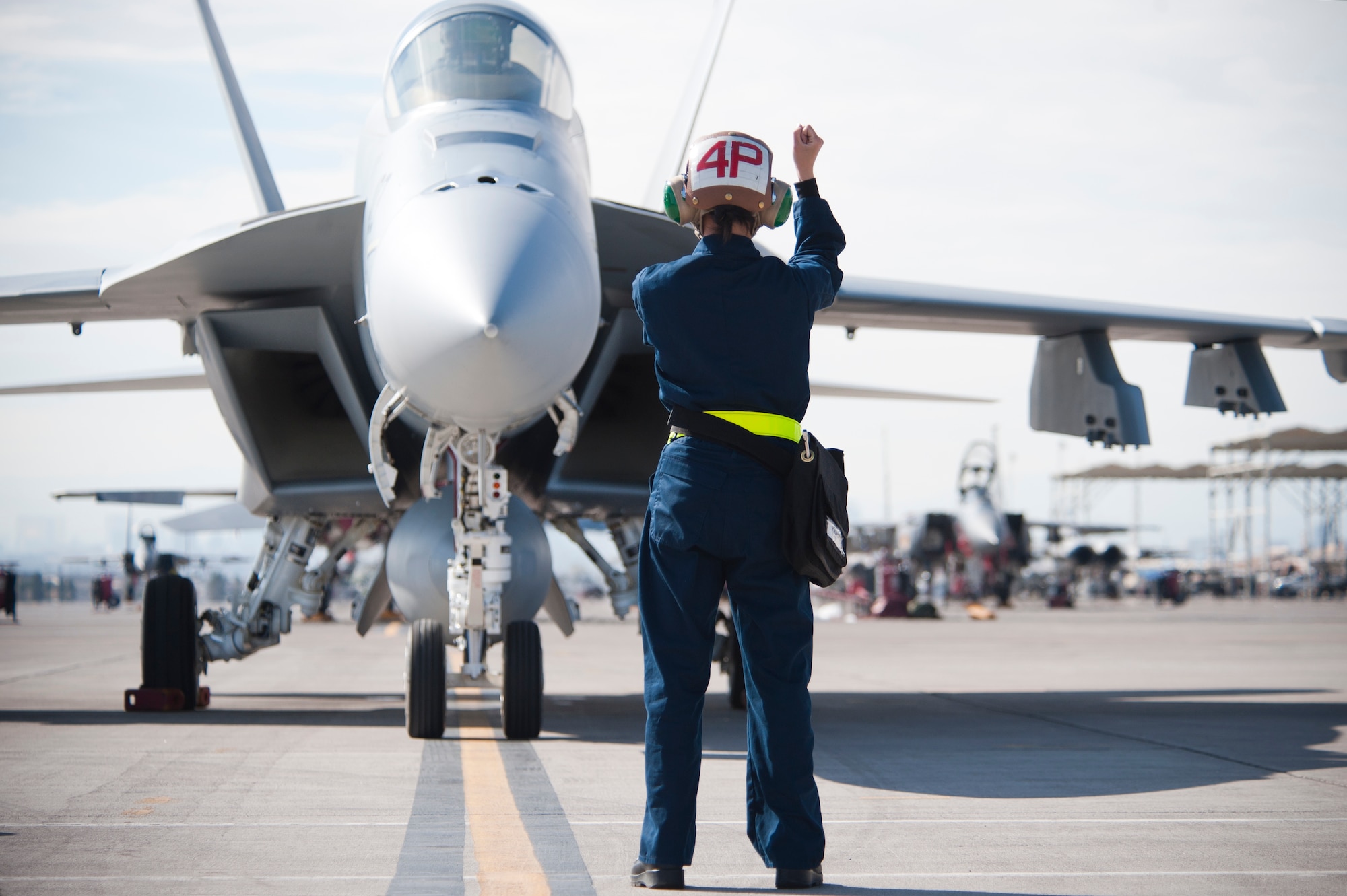 U.S. Navy Airman Zhou Chen, Strike Fighter Squadron 25 (VFA-25), Naval Air Station, Lemoore, Calif., plane captain, signals to an F/A18E Hornet pilot to hold prior to performing a pre-flight vertical rudder check on the Nellis Air Force Base, Nev. flight line Jan. 25, 2013. The VFA-25 is participating in Red Flag 13-2. Red Flag is a realistic combat training exercise involving joint and allied air forces. (U.S. Air Force photo by Lawrence Crespo)