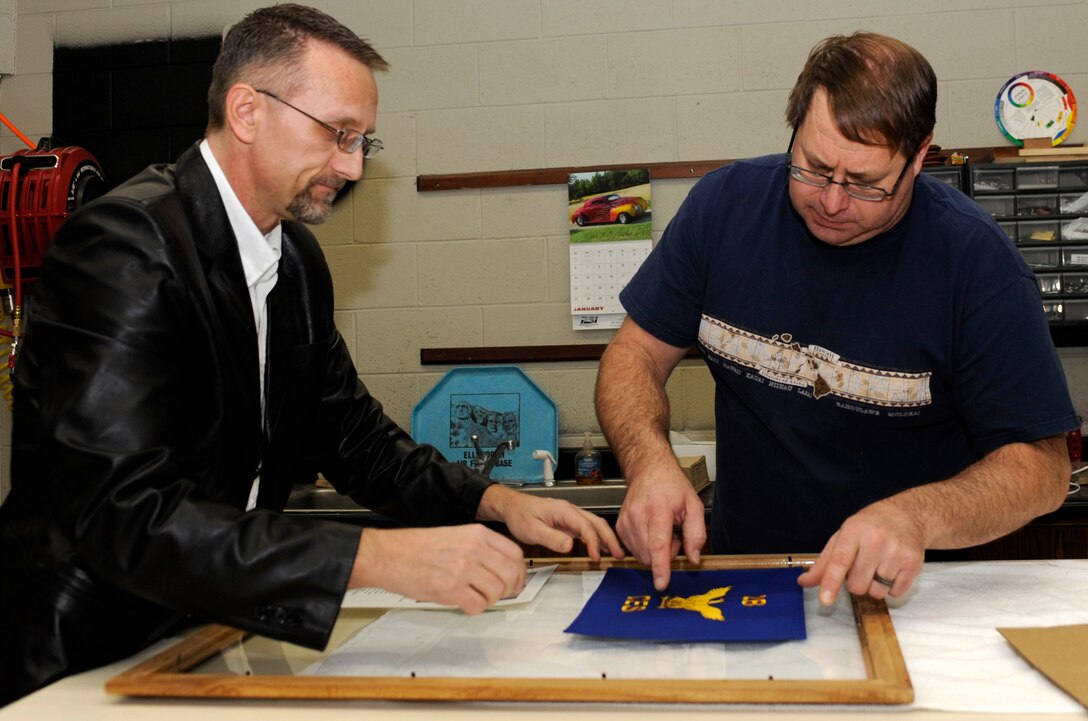 Travis Bolt (left), 28th Force Support Squadron Arts and Crafts center volunteer, and John Berry (right), 28th FSS Arts and Crafts center recreation assistant, lay out the design for a first sergeant's going away gift in the Arts and Crafts center at Ellsworth Air Force Base, S.D., Jan. 25, 2013. Air Combat Command selected the base's arts and crafts program as the best in ACC because of their innovative techniques and unique range of services for Airmen and their families. (U.S. Air Force photo by Airman Ashley J. Thum/Released) 