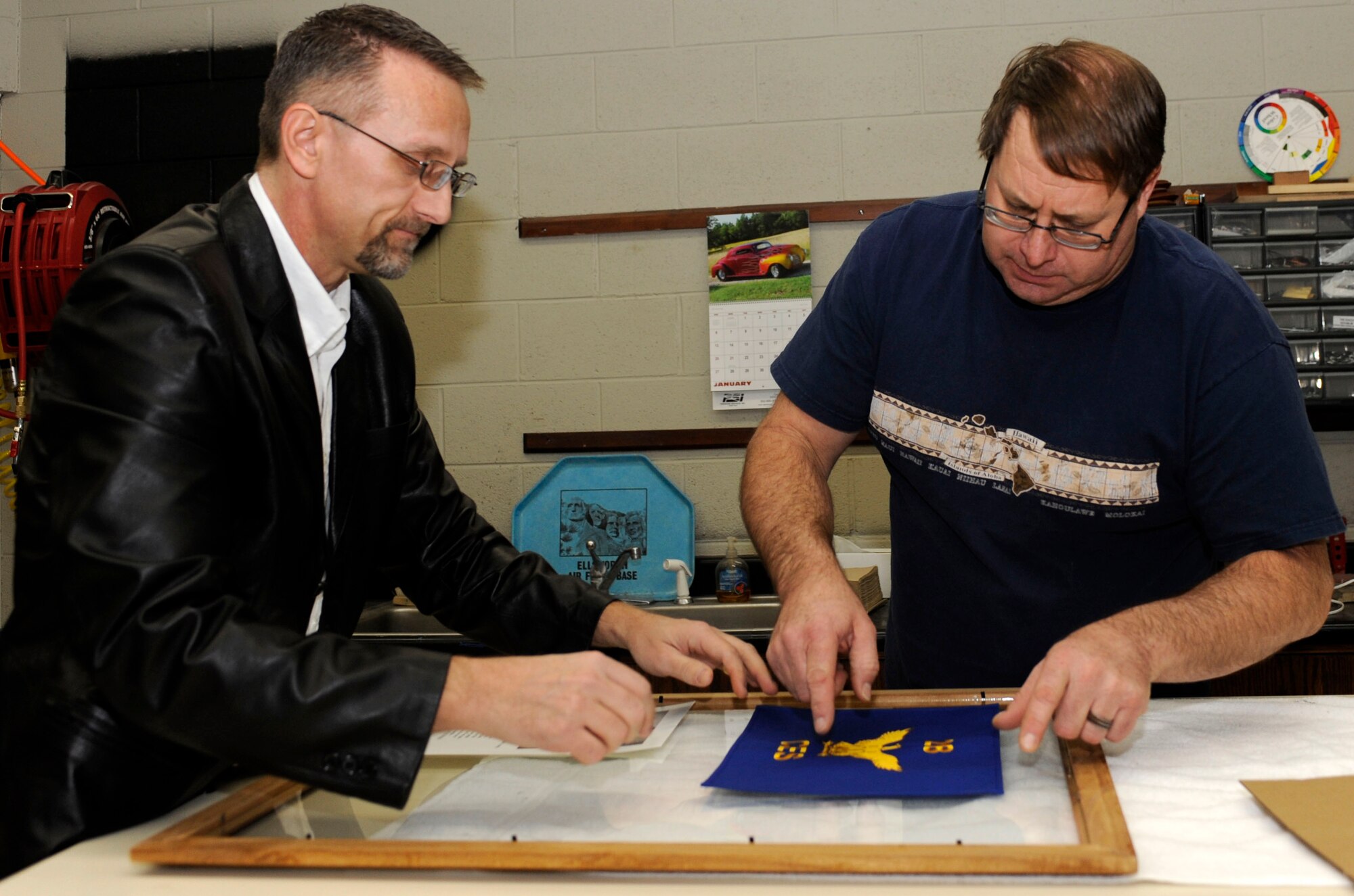 Travis Bolt (left), 28th Force Support Squadron Arts and Crafts center volunteer, and John Berry (right), 28th FSS Arts and Crafts center recreation assistant, lay out the design for a first sergeant's going away gift in the Arts and Crafts center at Ellsworth Air Force Base, S.D., Jan. 25, 2013. Air Combat Command selected the base's arts and crafts program as the best in ACC because of their innovative techniques and unique range of services for Airmen and their families. (U.S. Air Force photo by Airman Ashley J. Thum/Released) 