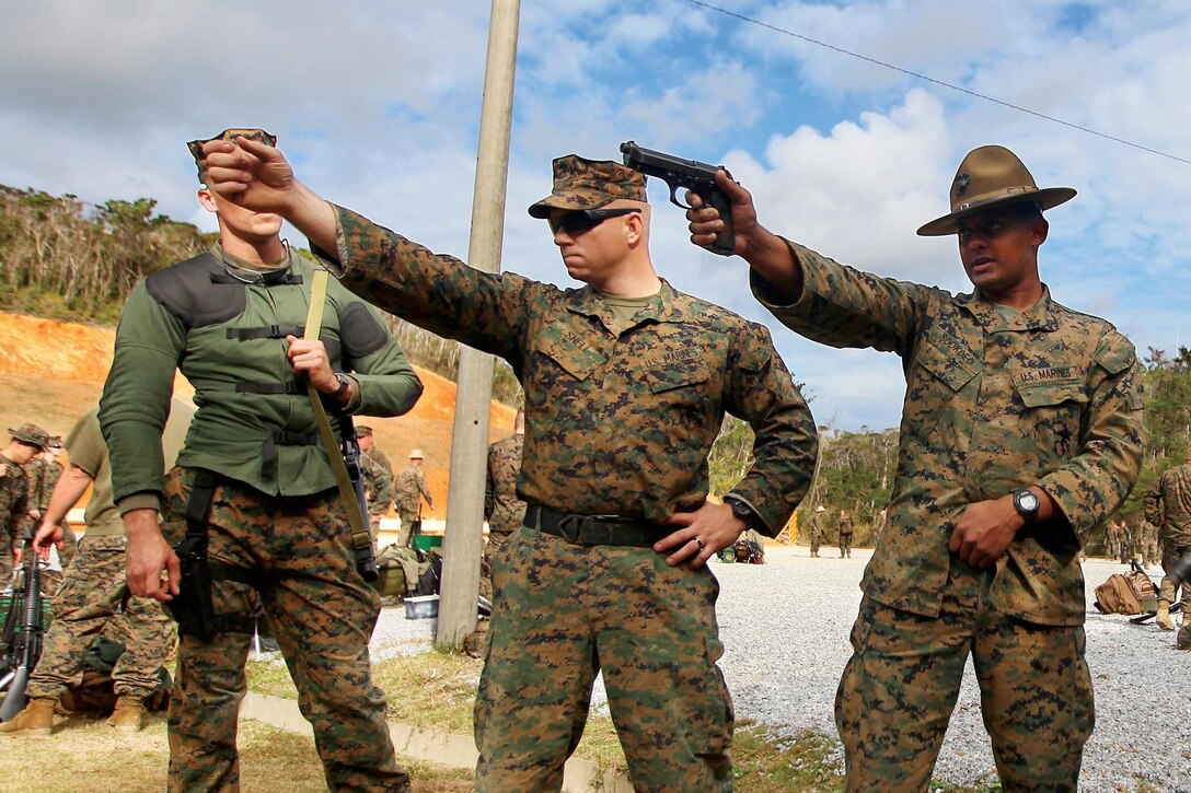 Cpl. Neil N. Sookdeo, center, teaches a shooter the proper pistol shooting position during the Far East Division Matches Jan. 23 at Camp Schwab. Over the course of the match, the Marine Corps Shooting Team taught Marines basic fundamentals such as trigger control, muscular relaxation, bone support, position, grip alignment, sight alignment and sight picture. Sookdeo is a small-arms weapons instructor with the Marine Corps Shooting Team. 