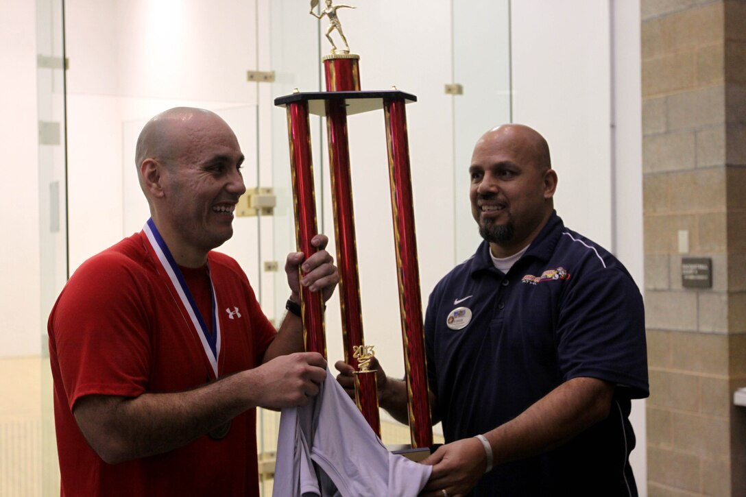 Gunnery Sgt. Jorge Polanco, an administrations chief for 1st Civil Affairs Group here, recieves a first place trophy for the Men's Novice Division from Eddie Bolanos, a sports recreation specialist with Semper Fit here, during one of the Commanding General's Cup Series racquetball tournaments here Jan. 30. 