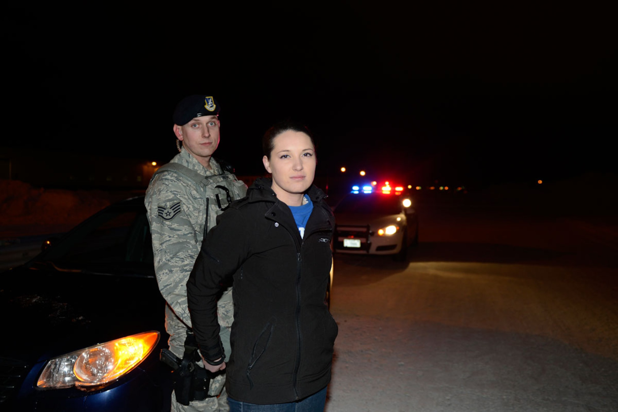 Air Force Staff Sgt. Daniel Phelps, 673d Security Forces Sqaudron, simulates arresting Airman 1st Class Carly Kavish, 673d Air Base Wing Wing Staff Agency, during a mock driving under the influence checkpoint. JBER has implemented periodic sobriety checkpoints for the installation in order to deter DUIs on base. (U.S. Air Force photo illustration/Airman 1st Class Omari Bernard)