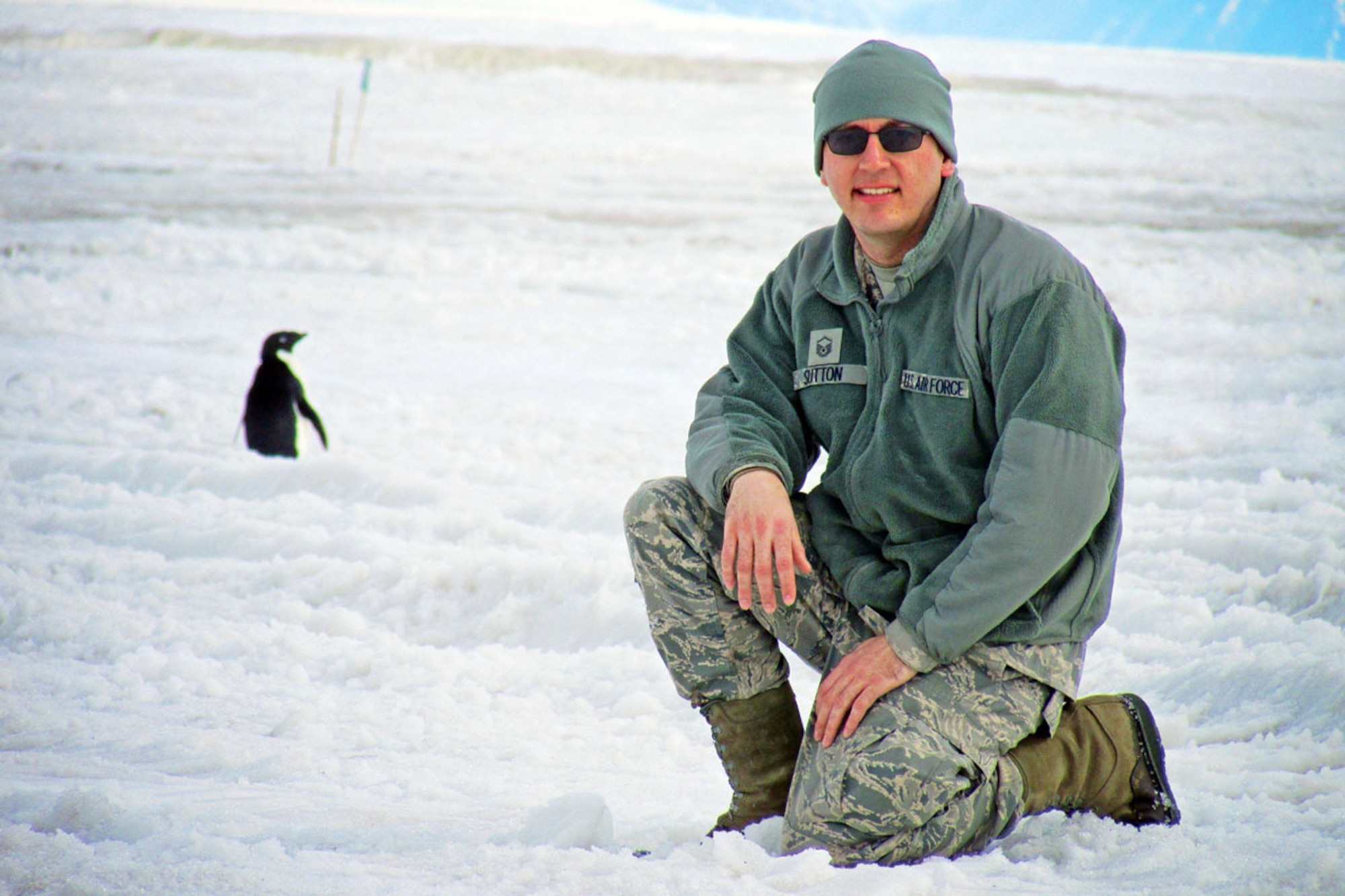 Air National Guard Master Sgt. Tyler Sutton, 176th Wing, Alaska Air National Guard, smiles while a penguin walks by the flight line near McMurdo Air Station, Antarctica. Sutton augmented the New York Air National Guard as an aircrew flight equipment specialist during a 30-day rotation in Antarctica supporting the National Science Foundation. (Courtesy photo)