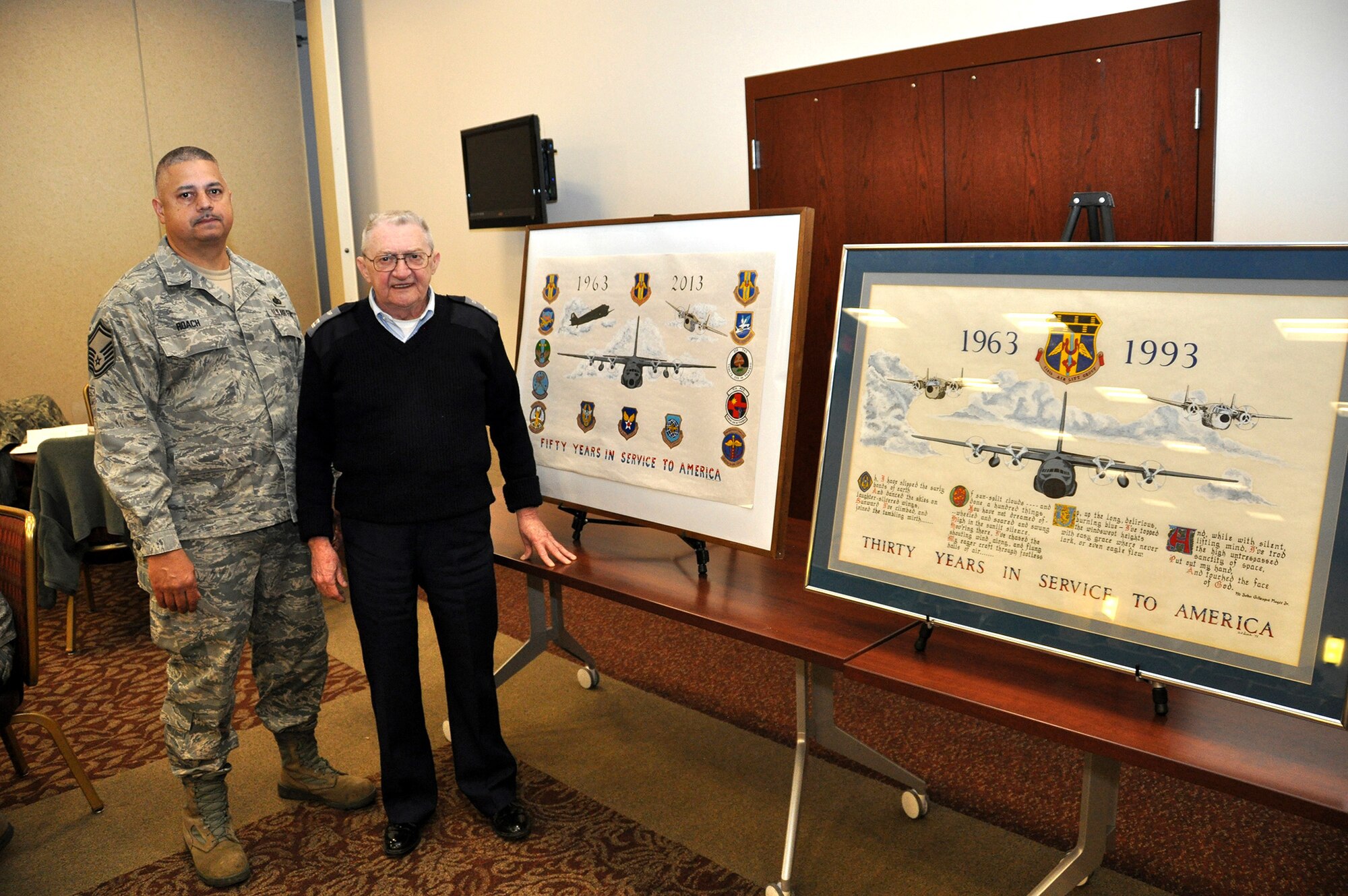 Capt. Ted Dodds (right), New York 116 Niagara Falls Squadron Composite #1 Civil Air Patrol, presents his latest historical artwork to base officials January 5, 2013 at the Niagara Falls Air Reserve Station, N.Y.  Dodd's artwork chronicles the 50th anniversary of the base and its rich history.  Displayed next to the current artwork is Dodds' previously donated painting done for Niagara's 30th anniversary.  Senior Master Sgt. Michael Roach (left), 914th Force Support Squadron Services Sustainment Flight, will display both paintings in a place of honor within the Heritage Center at Niagara.  (U.S. Air Force photo by Master Sgt. Kevin Nichols)