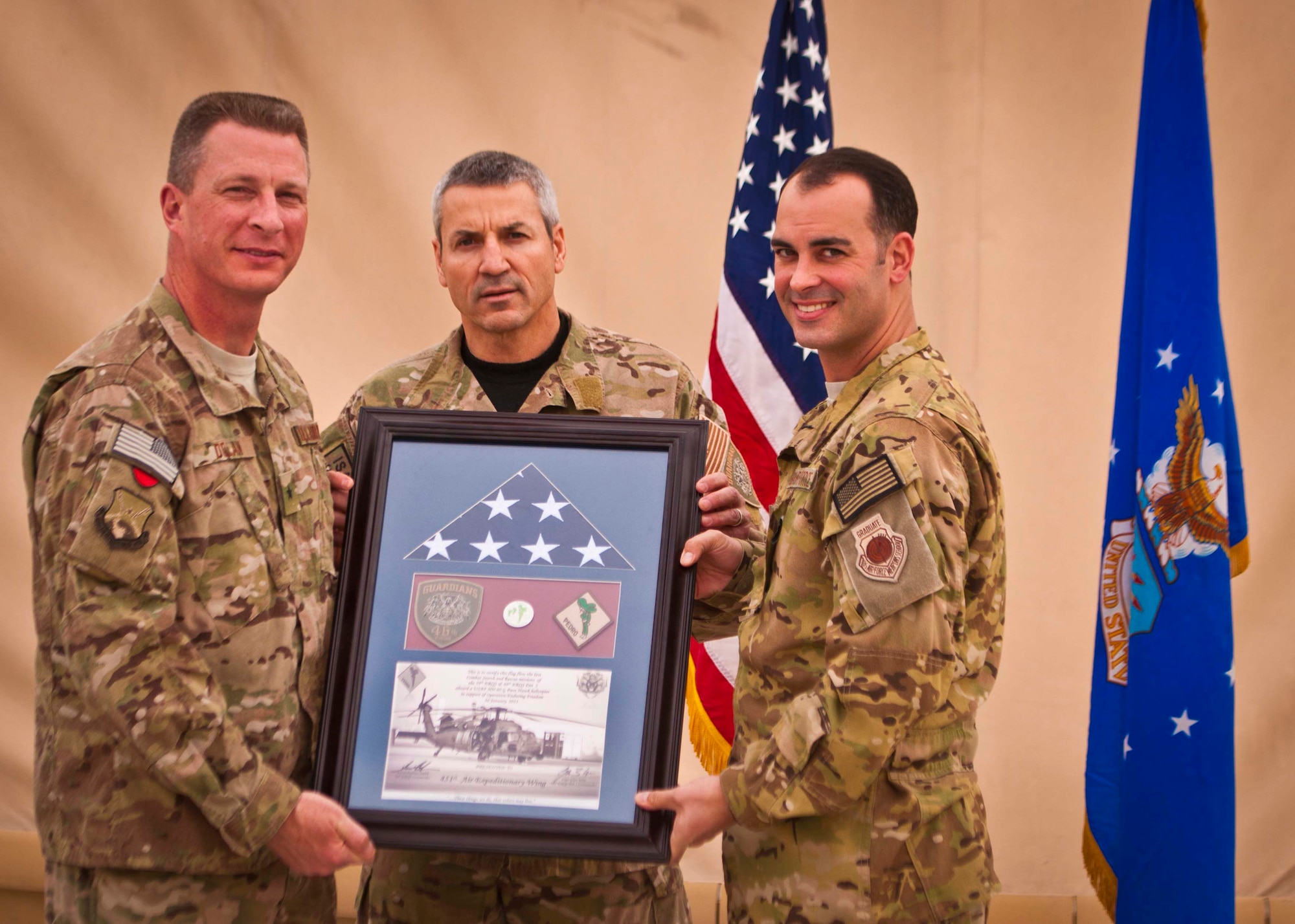 Brig. Gen. John Dolan, 451st Air Expeditionary Wing and Kandahar Airfield commander, accepts a plaque from Maj. Joseph Barnard, 46th Expeditionary Rescue Squadron commander, and Lt. Col. Andrew Smith, 59th ERQS commander, at a ceremony at KAF on Jan. 30. The ceremony marked the inactivation of the 46th ERQS, including a detachment at KAF, and the redeployment of the 59th ERQS, which will not be replaced. (U.S. Air Force photo/Senior Airman Scott Saldukas)