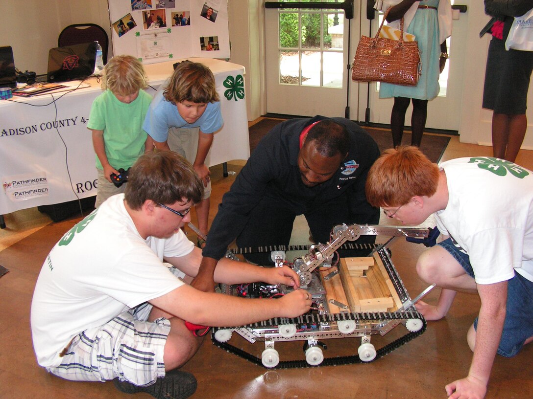 Dr. Patrick Taylor, center, an engineer at the Aviation and Missile Research Development and Engineering Center, explains robotic principles to Madison County 4-H Robotics team members during the Tennessee Valley Jazz Society’s Science and Arts Symposium. 