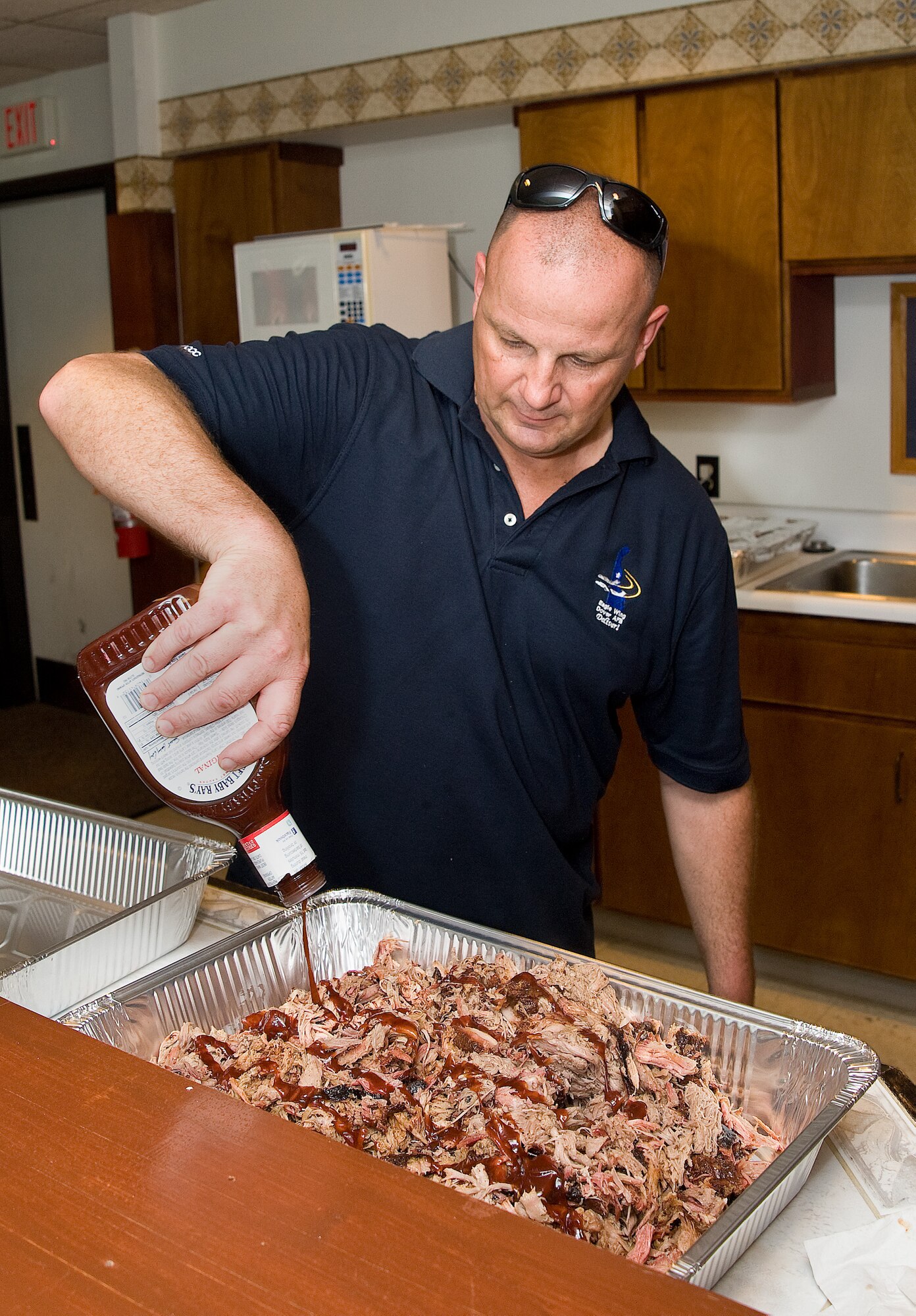 Chief Master Sgt. Jim Smith, 436th Airlift Wing command chief, pours barbeque sauce on a tray of pulled pork barbeque June 26, 2013, at the Eagle?s Net Caf? on Dover Air Force Base, Del. Smith cooked more than 110 pounds of barbeque for dorm residents. (U.S. Air Force photo/Roland Balik)