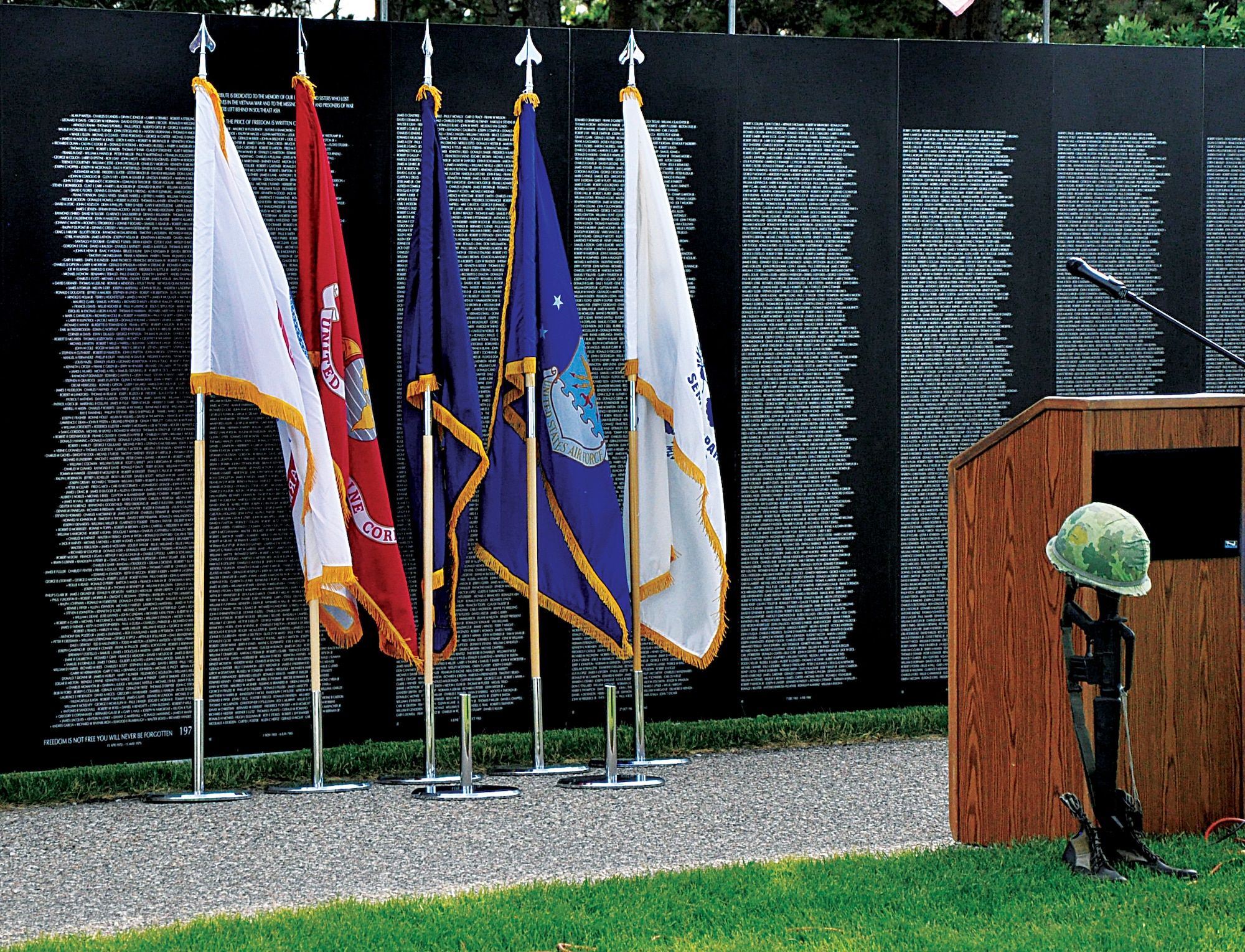 Military branch flags and a battle cross are posted in front of the Traveling Vietnam Memorial Wall before the opening ceremony held in Lions Park, Cheyenne, Wyo., June 20, 2013. (U.S. Air Force photo by Senior Airman Mike Tryon)