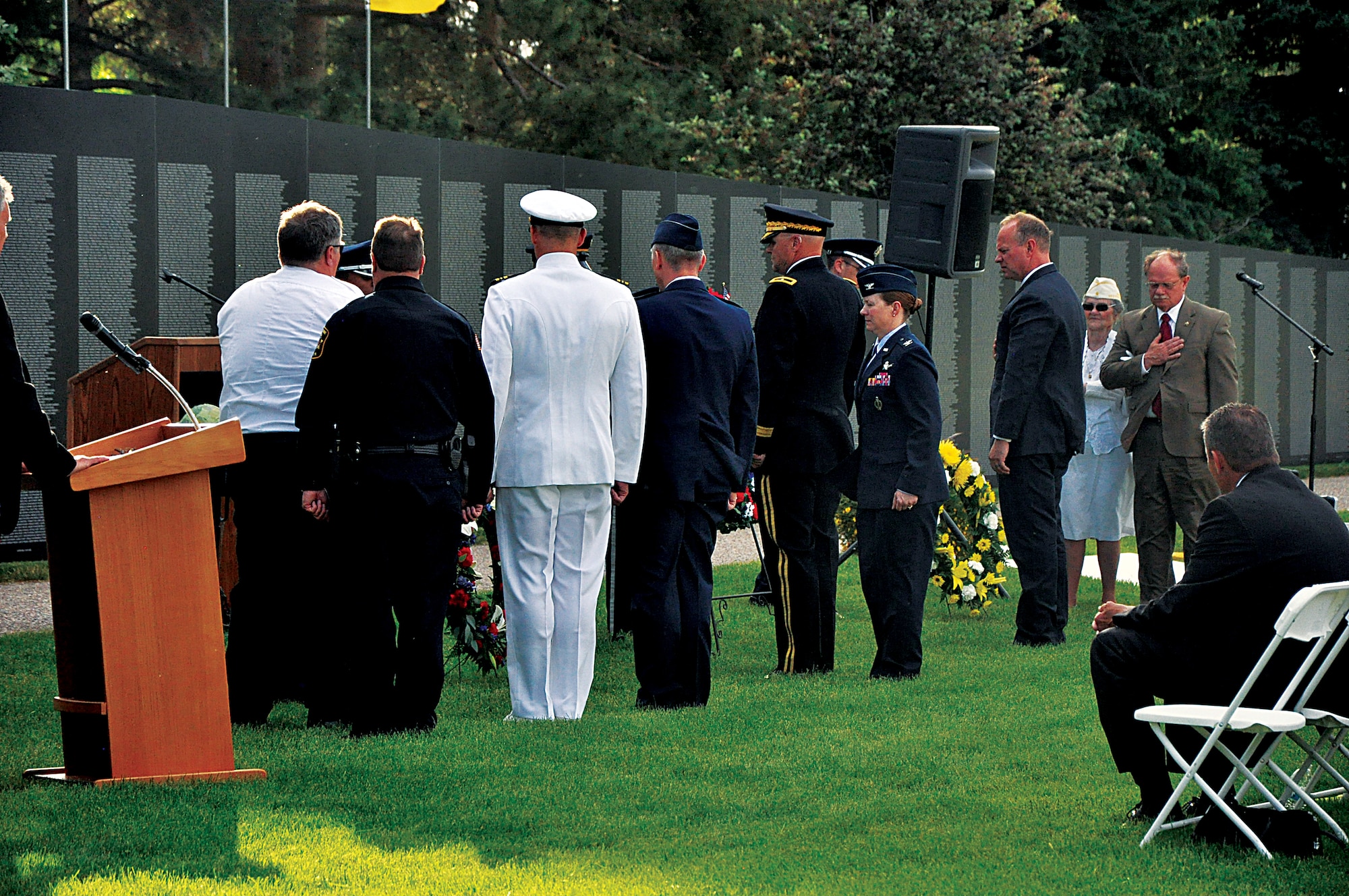 Wyoming’s military and civilian leaders stand somberly after placing wreaths in front of the Traveling Vietnam Memorial Wall, which was being displayed in Lions Park, Cheyenne, Wyo., from June 20 through June 23, 2013, as a bag-piper plays “Amazing Grace” during the opening ceremony. (U.S. Air Force photo by Senior Airman Mike Tryon)