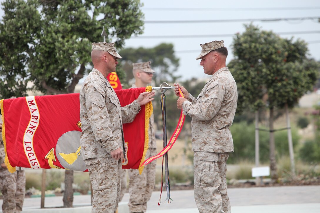 Brigadier Gen. John J. Broadmeadow, right, commanding general, 1st Marine Logistics Group, attaches battle streamers to 1st MLG’s 
battle colors during the unit’s 66th anniversary aboard Camp Pendleton, Calif., July 1, 2013. The Marines and sailors of 1st MLG have participated in every engagement involving the Marine Corps since the Korean War.