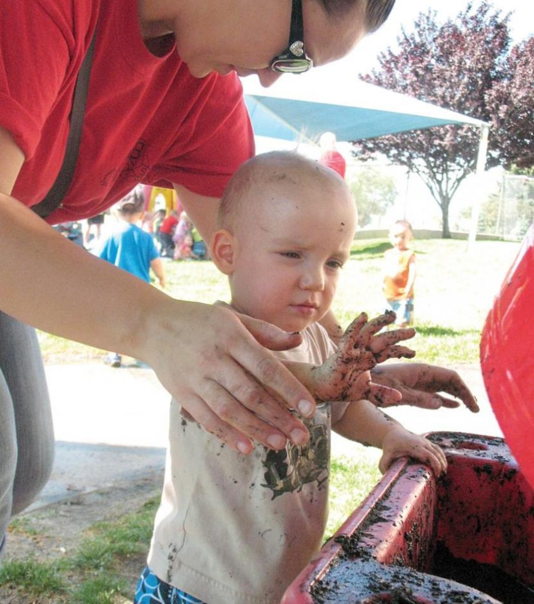 Joshua Keslar is assisted by Megan Brunner as he finishes up play in a sensory table filled with mud. The Hill Air Force Base, Utah, Child Development Center celebrated International Mud Day June 28. (Courtesy photo by Mary Lou Gorny)
