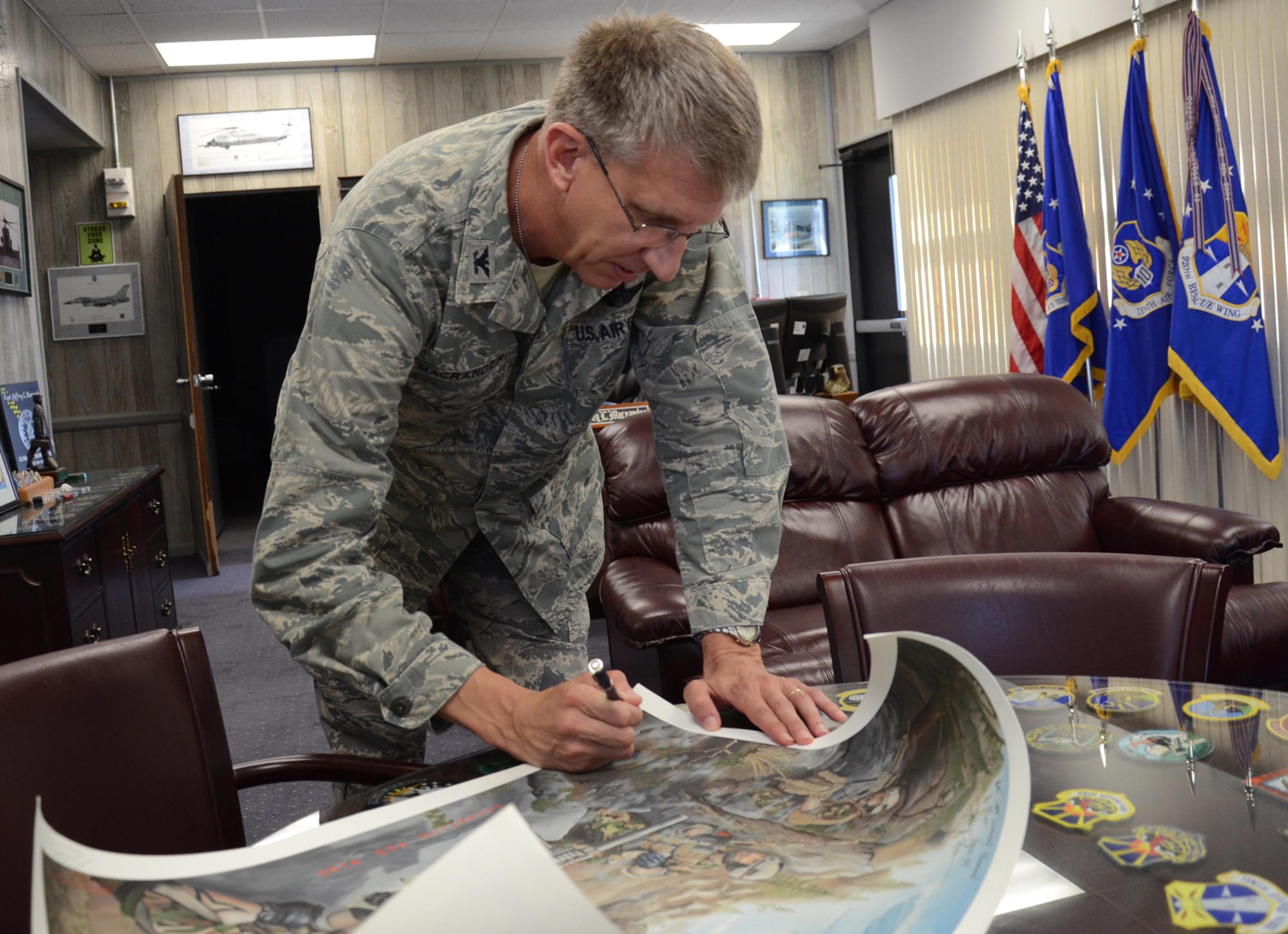 Col. Jeffrey Macrander signs an artist's rendition of Operation Redwing. The image shows four Navy SEALs who initiated the operaton engaged in a firefight by Jason Nicholson 2011. Macrander and fellow rescuers from the 920th Rescue Wing were part of the rescue mission that brought Navy SEAL Marcus Luttrell, the lone survivor of the operaton, home. (U.S. Air Force photo/Master Sgt. Paul Flipse)