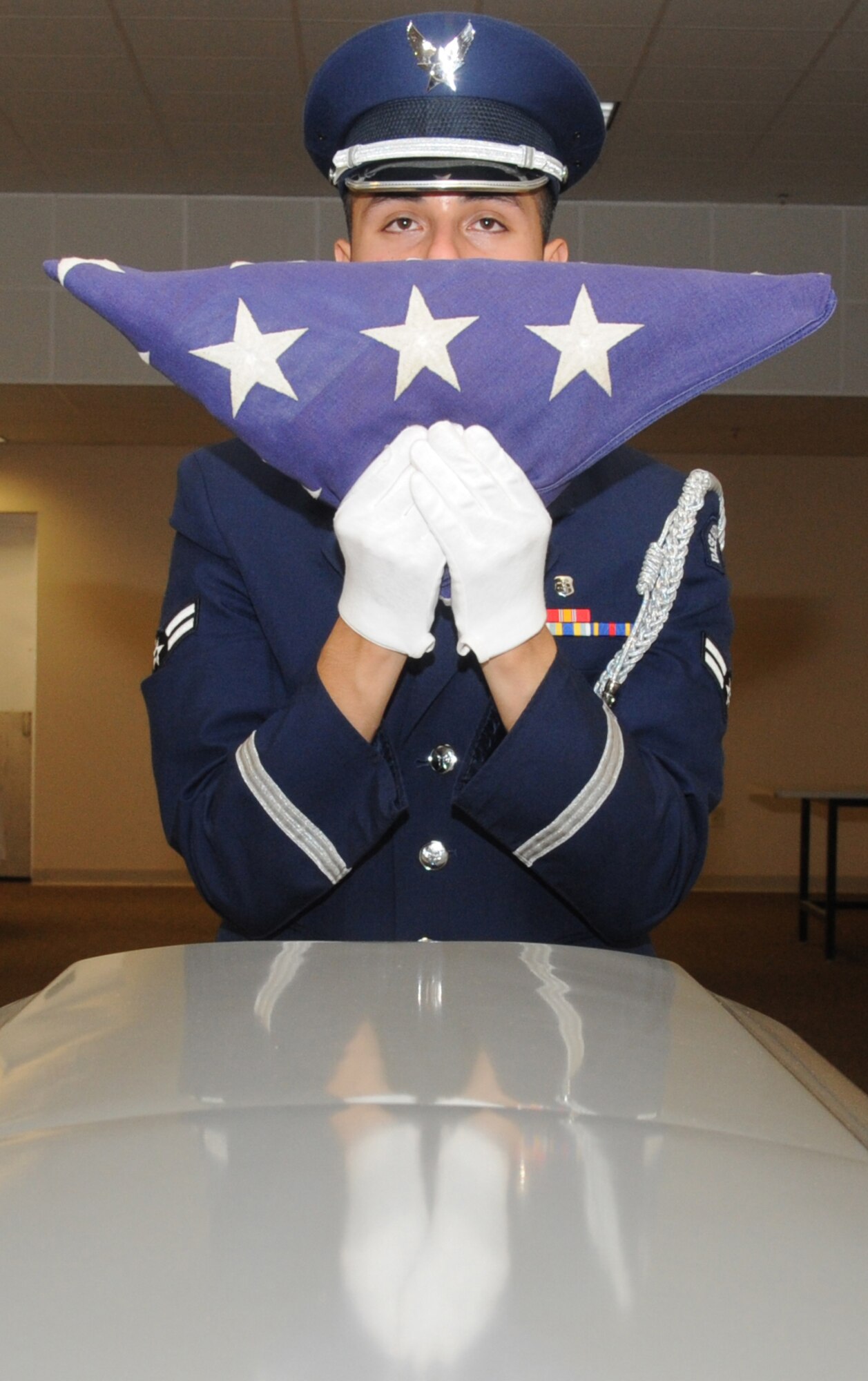 Airman 1st Class Pedro Ayala, Keesler Honor Guard member, stands in front of a casket while preparing the American flag for presentation to a family member of the deceased during a training session June 26, 2013, at the Locker House, Keesler Air Force Base, Miss. The Keesler Honor Guard’s primary mission is to render military honors for our nation’s fallen service members.  They also support other ceremonial functions such as saber/sword cordons, parades, posting of the colors at retirements, change of commands, prisoner of war/missing in action honors, weddings, sporting events and venues within the local community.  (U.S. Air Force photo by Kemberly Groue)