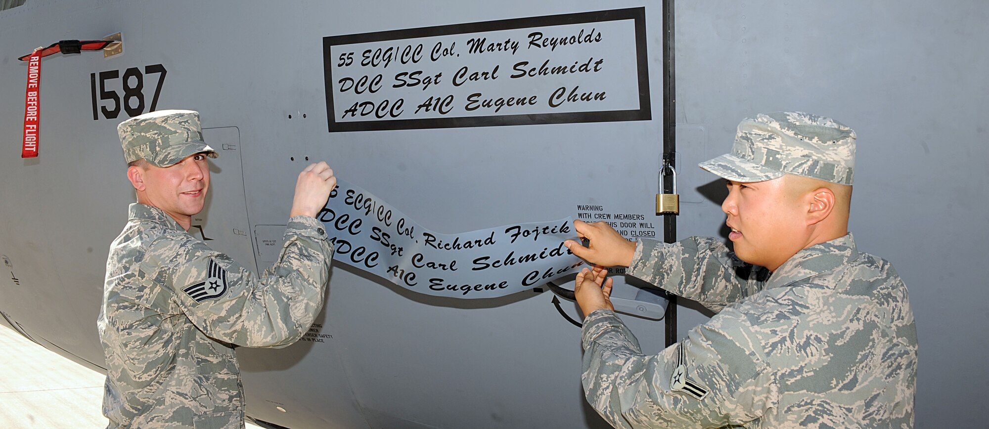 U.S. Air Force Staff Sgt. Carl Schmidt, 755th Aircraft Maintenance Squadron, and Airman 1st Class Eugene Chun, 43rd Electronic Combat Squadron, unveil the name of Col. George Reynolds on an EC-130H Compass Call aircraft June 27 at Davis-Monthan Air Force Base. Reynolds assumed command of the 55th Electronic Combat Group at D-M. (U.S. Air Force photo by Senior Airman Timothy Moore/Released)