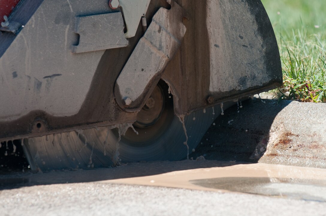 Heavy equipment and pavement technicians from the 28th Civil Engineer Squadron use a concrete saw to cut through a curb during minor repairs in front of the 28th Bomb Wing Headquarters building on Ellsworth Air Force Base, S.D., June 27, 2013. The saw uses water to cool the blade during operation to prevent overheating, allowing for a precise cut. (U.S. Air Force photo by Senior Airman Kate Maurer/Released) 