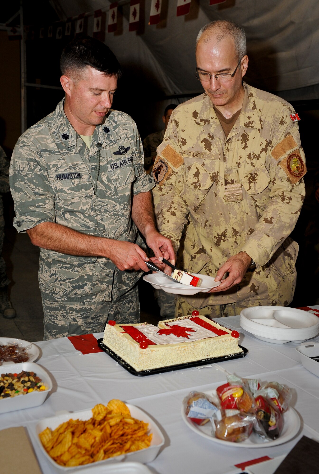 U.S. Air Force Lt. Col. Darin Humiston gives Canadian Air Forces Maj. Mike Hagen a piece of cake during the Canada Day celebration at the 379th Air Expeditionary Wing in Southwest Asia, July 1, 2013. Humiston is the U.S. Air Force 71st Expeditionary Air Control Squadron commander and Hagen is the Canadian 71st EACS commander. Deployed service members shared in activities ranging from a Canadian trivia game, guitar solo and board games. (U.S. Air Force photo/Senior Airman Benjamin Stratton)