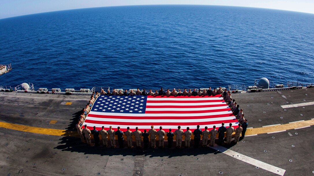 U.S. Marines and Sailors assigned to the 26th Marine Expeditionary Unit (MEU), and Sailors assigned to the USS Kearsarge (LHD 3), hold the American flag to commemorate the Fourth of July during their 2013 deployment on the flight deck of the USS Kearsarge, at sea, July 4, 2013.  The 26th MEU is a Marine Air-Ground Task Force forward-deployed to the U.S. 5th Fleet area of responsibility aboard the Kearsarge Amphibious Ready Group serving as a sea-based, expeditionary crisis response force capable of conducting amphibious operations across the full  range of military operations. (U.S. Marine Corps photograph by Sgt. Christopher Q. Stone, 26th MEU Combat Camera/Released) 
