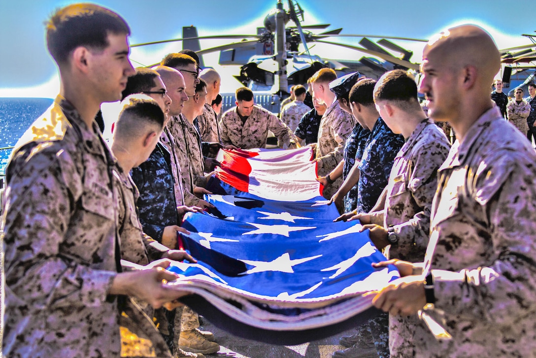 U.S. Marines and Sailors assigned to the 26th Marine Expeditionary Unit (MEU),and Sailors assigned to the USS Kearsarge (LHD 3), fold the American flag to commemorate the Fourth of July during their 2013 deployment on the flight deck of the USS Kearsarge, at sea, July 4, 2013.  The 26th MEU is a Marine Air-Ground Task Force forward-deployed to the U.S. 5th Fleet area of responsibility aboard the Kearsarge Amphibious Ready Group serving as a sea-based, expeditionary crisis response force capable of conducting amphibious operations across the full  range of military operations. (U.S. Marine Corps photo by Cpl. Kyle N. Runnels/Released) (This image was created using high dynamic range techniques: 130704-BS001-M-024: 130704-BS001-M-025: 130704-BS001-M-026)