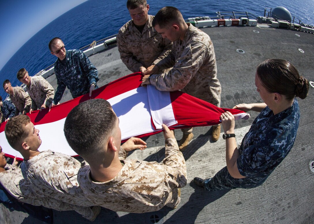 U.S. Marines and Sailors assigned to the 26th Marine Expeditionary Unit (MEU), and Sailors assigned to the USS Kearsarge (LHD 3), fold the American flag to commemorate the Fourth of July during their 2013 deployment on the flight deck of the USS Kearsarge, at sea, July 4, 2013.  The 26th MEU is a Marine Air-Ground Task Force forward-deployed to the U.S. 5th Fleet area of responsibility aboard the Kearsarge Amphibious Ready Group serving as a sea-based, expeditionary crisis response force capable of conducting amphibious operations across the full  range of military operations. (U.S. Marine Corps photograph by Sgt. Christopher Q. Stone, 26th MEU Combat Camera/Released)