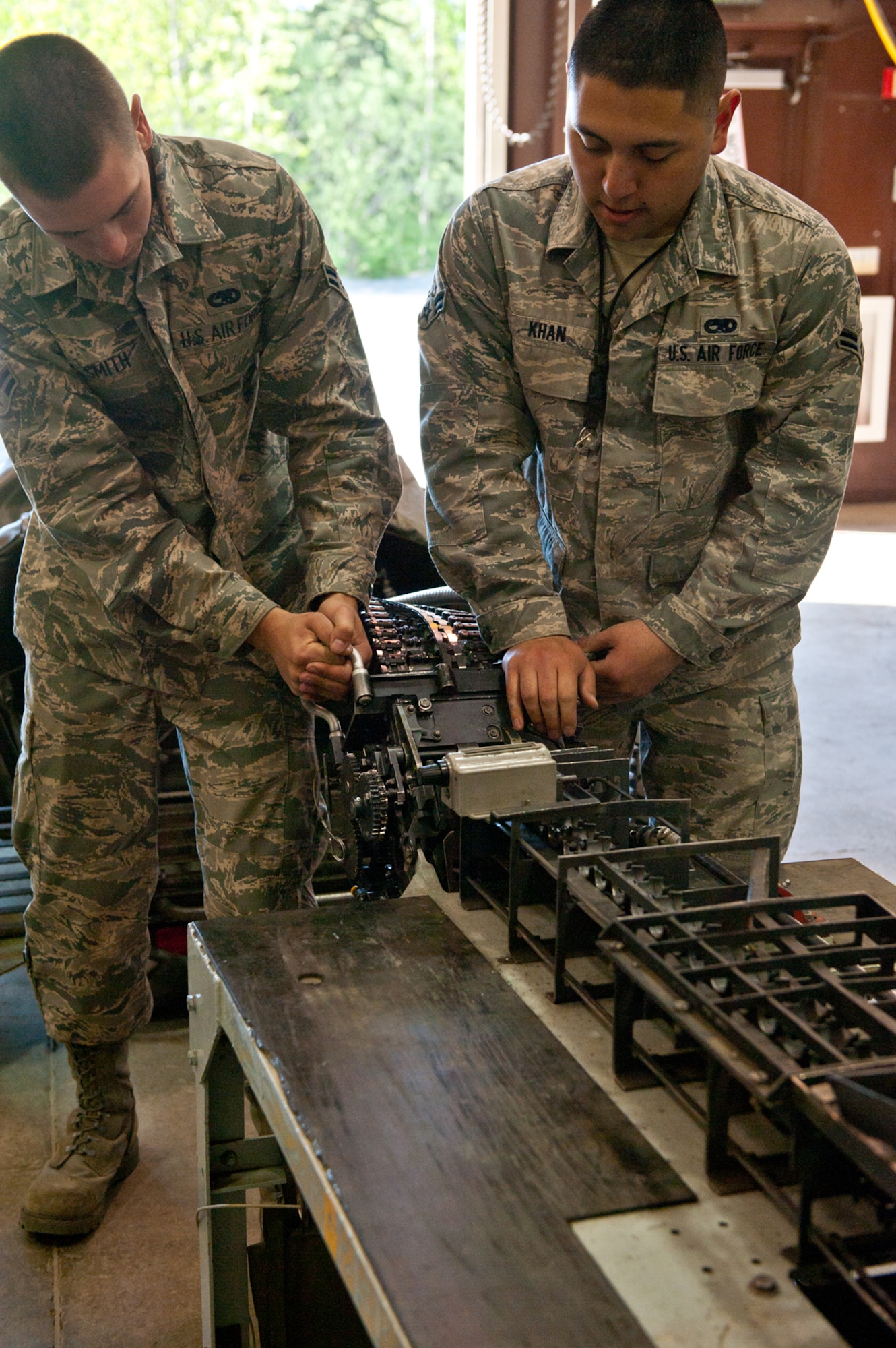 JOINT BASE ELMENDORF-RICHARDSON, Alaska - - Airman 1st Class Cody Smith and Airman 1st Class Jumah Khan, assigned to the 3rd Munitions Squadron, Conventional Munitions Crew Members in Production Flight, are attaching the Universal Ammunition Loading System to the replenisher table, June 7, 2013.  (U.S. Air Force photo/Johnathon Green)