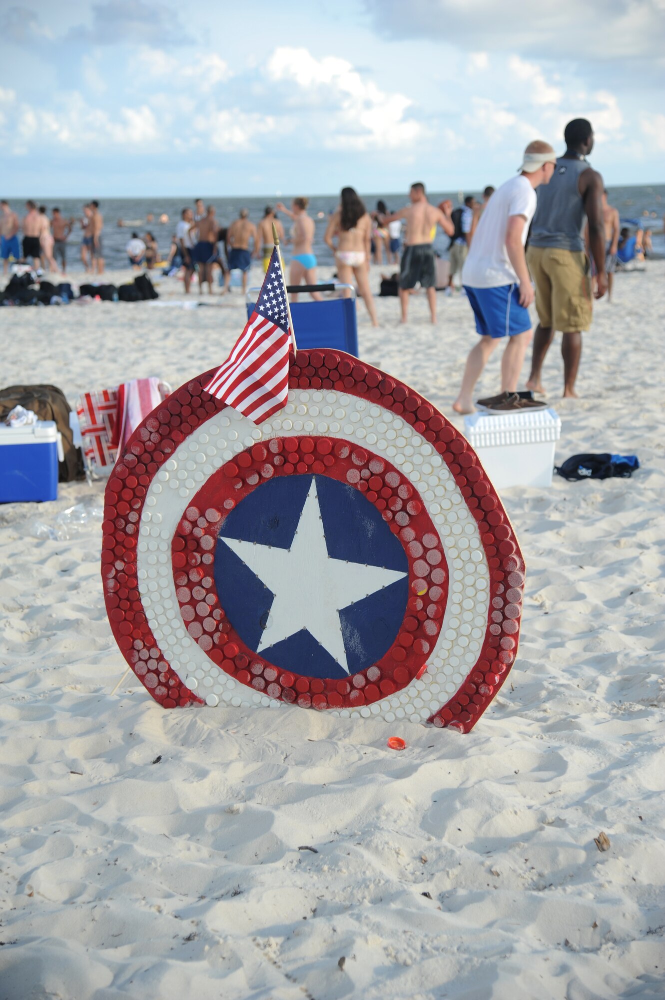 A Captain America, the Marvel super hero, shield sits in the sand on the beach with Keesler Airmen in the background during Keesler’s 4th of July Beach Bash, July 4, 2013, on the Biloxi Beach.  The event, held in honor of our nation’s Independence Day, included food, games, music, contests and fireworks.  (U.S. Air Force photo by Kemberly Groue)