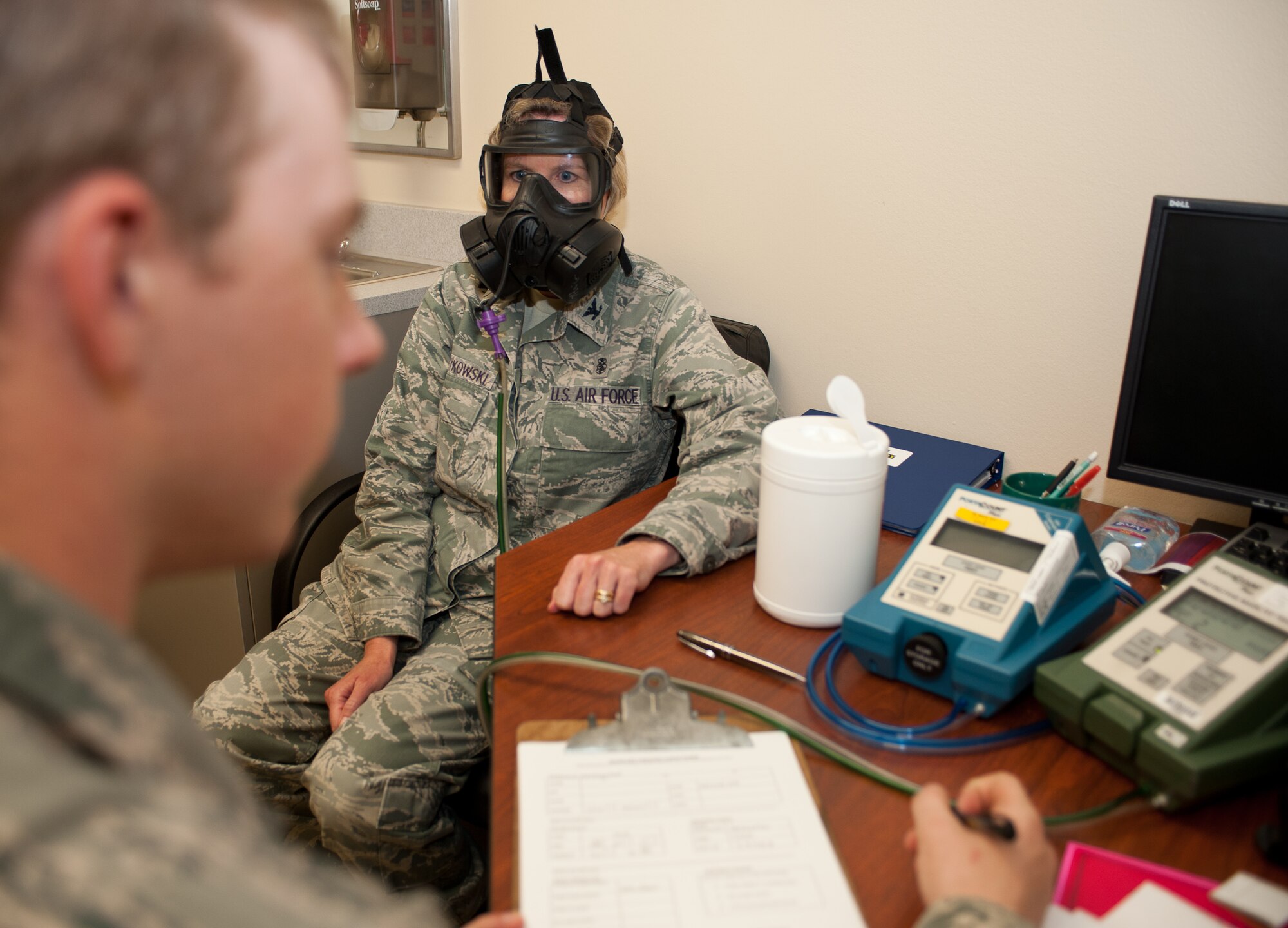 Col. Susan Pietrykowski, 28th Medical Group commander, performs deep breathing during a gas mask fit test as Airman 1st Class Zachary Piper, 28th Medical Operations Squadron bioenvironmental engineering technician, evaluates the amount of oxygen that is maintained in the mask at Ellsworth Air Force Base, S.D., July 1, 2013. The fit test uses two hoses, one connected to the drinking hose to the interior of the mask and the other used to measure the ambient air on the outside, allowing a technician to assesses how many particles of oxygen are retained in the mask. (U.S. Air Force photo by Airman 1st Class Alystria Maurer/Released)