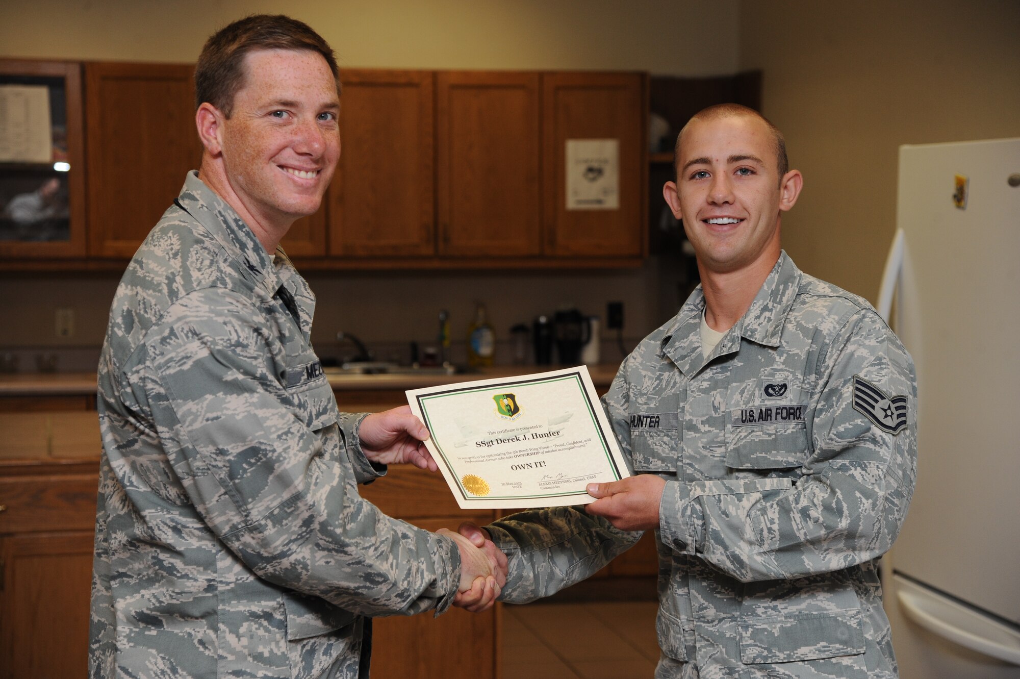 Col. Alexis Mezynski, 5th Bomb Wing commander, presents the OWN IT award to Staff Sgt. Derek Hunter, 5th Civil Engineer Squadron, here, July 1 , 2013. Sergeant Hunter has epitomized the 5th BW commander’s vision of mission ownership.  He was the lead craftsman responsible for the innovative solution planning and installation of the heating, ventilation and air conditioning direct digital controls at JR Rockers. This project saved $50,000 in contract costs and paved the way for the advanced HVAC technology to be installed across the installation. The DDC system will enable technicians to remotely access, monitor and troubleshoot temperature and humidity controls from a centralized location, saving 480 man-hours and 220,000 kilowatts in energy annually. His hard work and leadership set the foundation to expand the development of this technology to seven additional buildings on base.  Finally, Hunter has quickly become the foremost DDC expert and diligently trained 35 military personnel in this high-tech discipline. Congratulations Sergeant Hunter for OWNing your mission. (U.S. Air Force photo/Airman 1st Class Andrew Crawford)