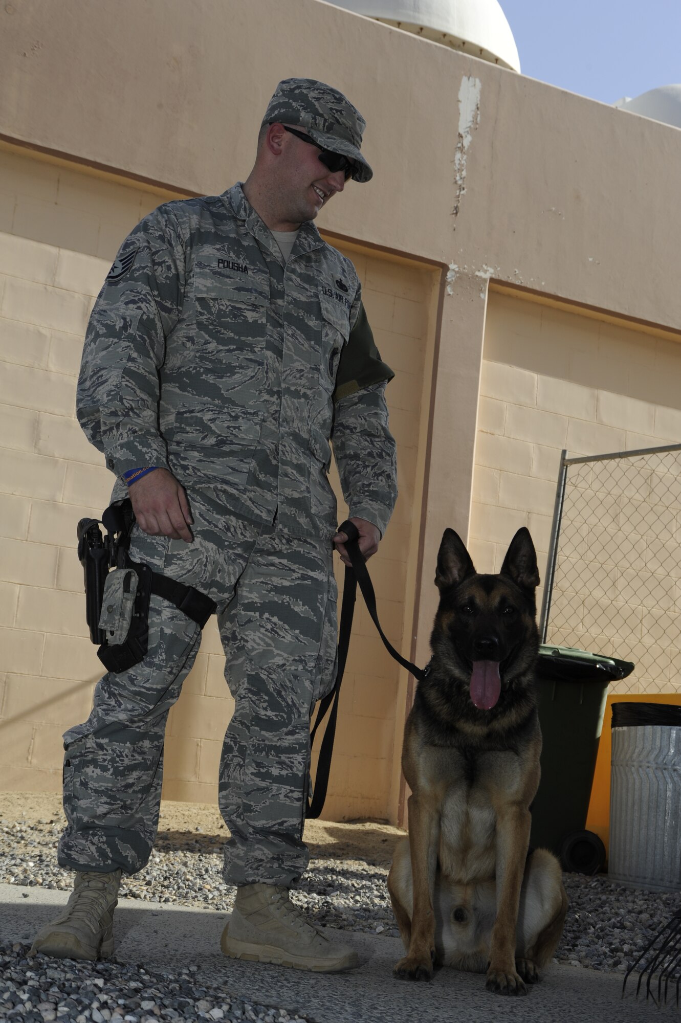 Staff. Sgt. Bradley Pousha, 386th Expeditionary Security Forces Squadron military working dog handler, stands with Lenin, 386th ESFS MWD here, July 2. Pousha and Lenin are getting ready to check all vehicles coming into the base for unauthorized contraband items.  MWDs provide another level of security for the service members who work on the installation.  Pousha and Lenin are both deployed from Joint Base San Antonio, Texas.  (U.S. Air Force photo by Master Sgt. Christopher A. Campbell)