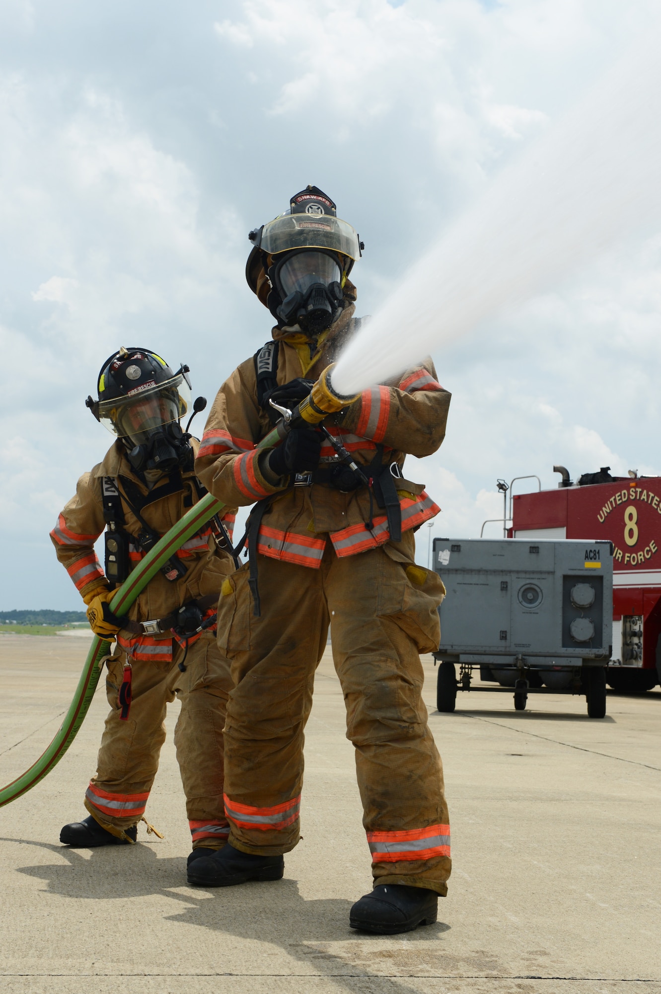 Airman 1st Class Harvey Cooper and Senior Airmen Brandon Young, 20th Civil Engineer Squadron firefighters, practice spraying one of the hoses on their fire truck at Shaw Air Force Base, S.C., July 9, 2013. The hose is able to spray out 100 pounds of water per minute.(U.S. Air Force photo by Airman 1st Class Krystal M. Jeffers/Released)