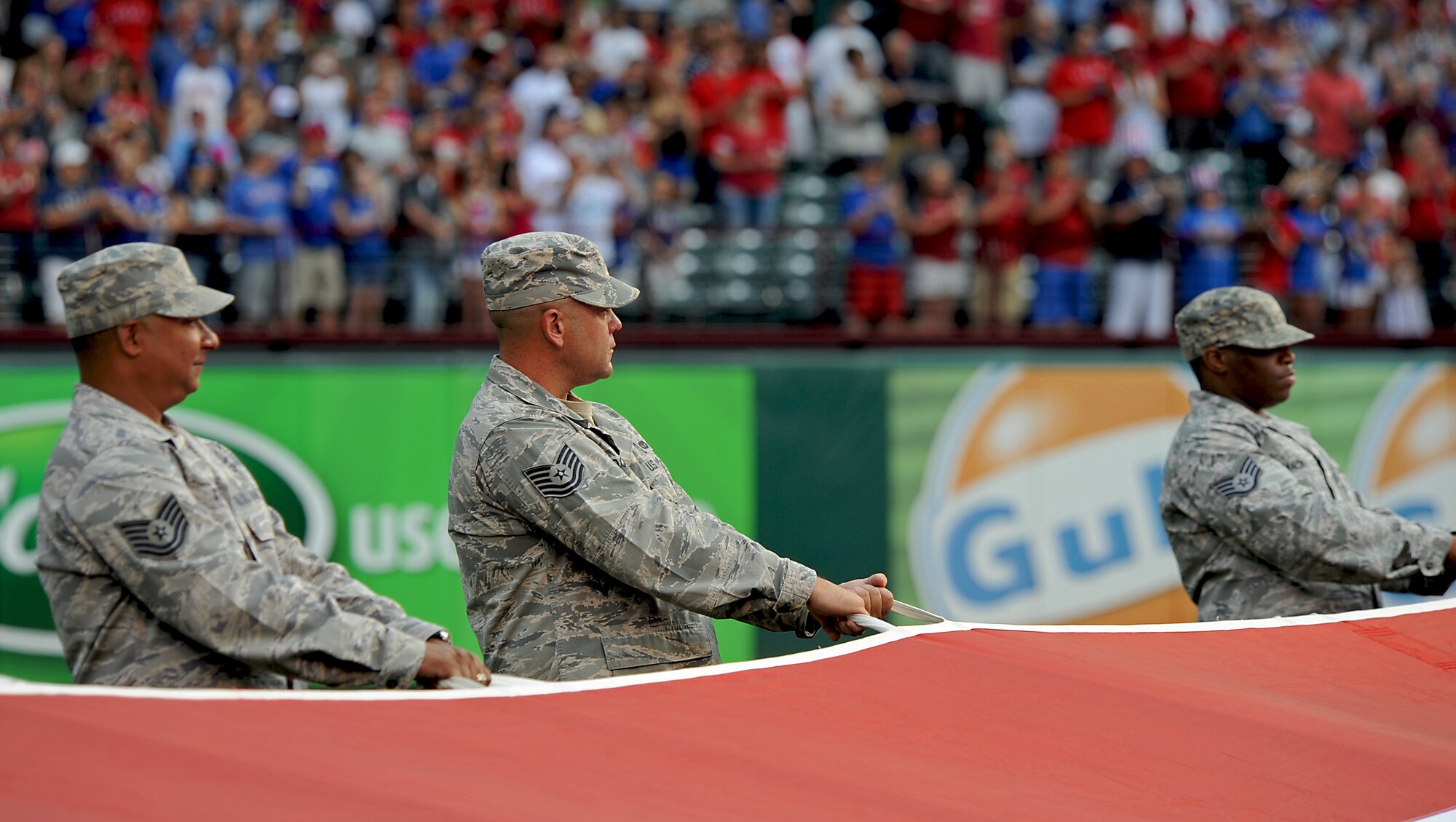 U.S. Air Force Tech. Sgt. Craig Cooper, 7th Civil Engineer Squadron, Dyess Air Force Base, Texas, center, holds an American flag July 4, 2013, at Rangers Ballpark in Arlington, Texas during his stepdaughter’s Air Force enlistment ceremony, prior to a Texas Ranger’s baseball game. (U.S. Air Force photo by Airman 1st Class Peter Thompson/Released)