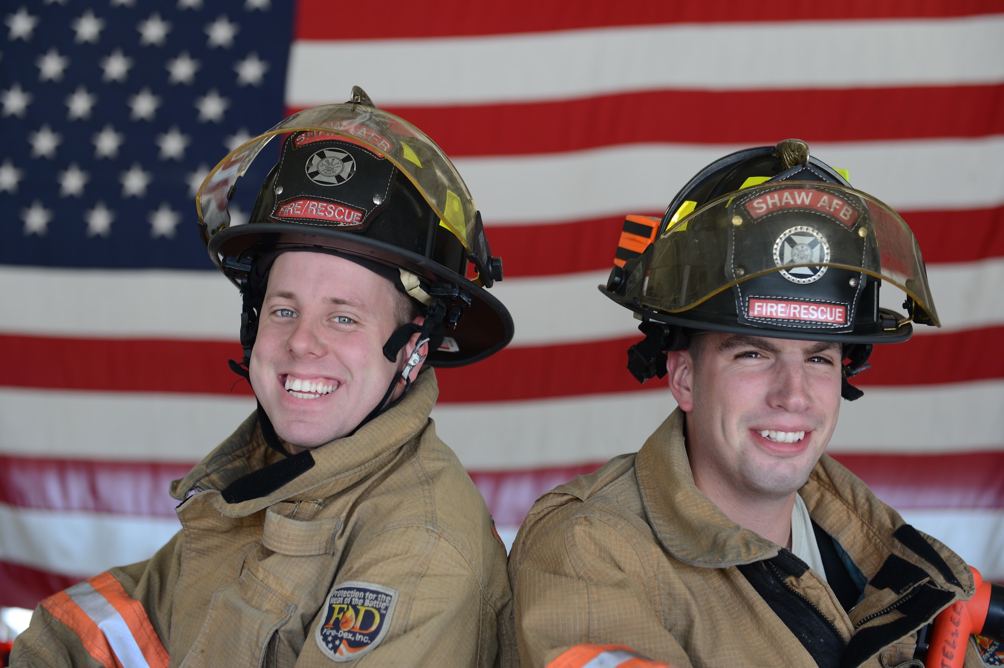 Senior Airmen Phillip Statzer and Jeremy Brannock, 20th Civil Engineer Squadron firefighters, pose in front of the American flag at Shaw Air Force Base, S.C., July 8, 2013. The suits they wear to protect themselves from burns, called structural gear, weigh about 50 pounds. (U.S. Air Force photo by Airman 1st Class Krystal M. Jeffers/Released)