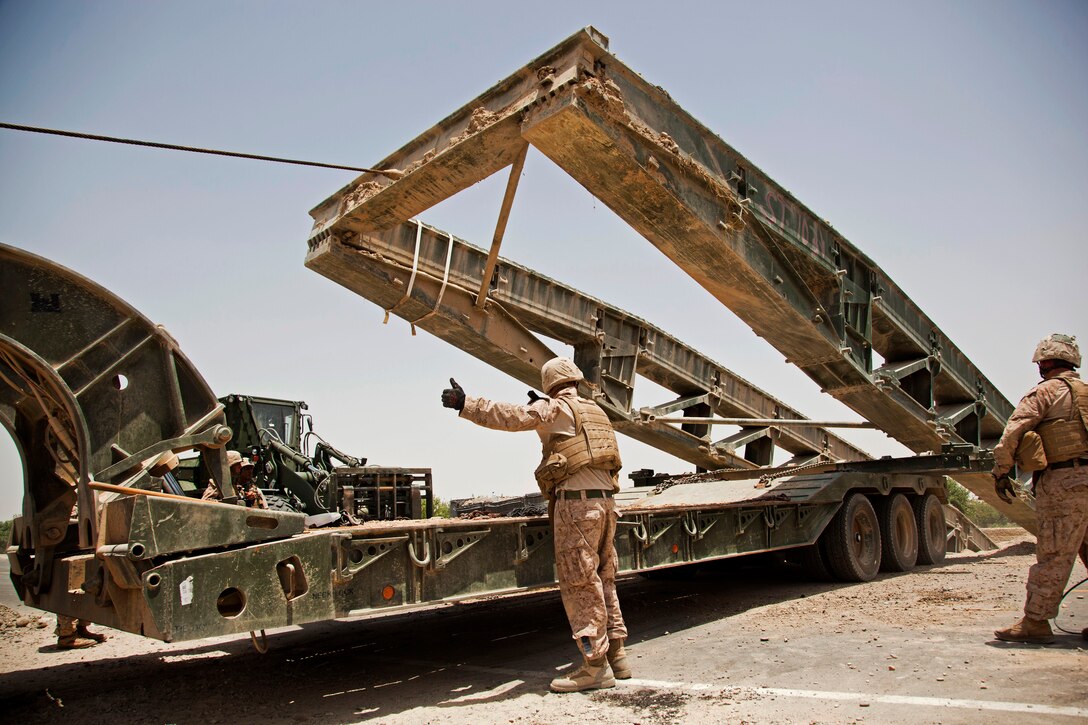 A U.S. Marine provides direction as a medium girder bridge is loaded onto a flatbed truck in Lashkar Gah City in Afghanistan’s Helmand province, June 29, 2013.