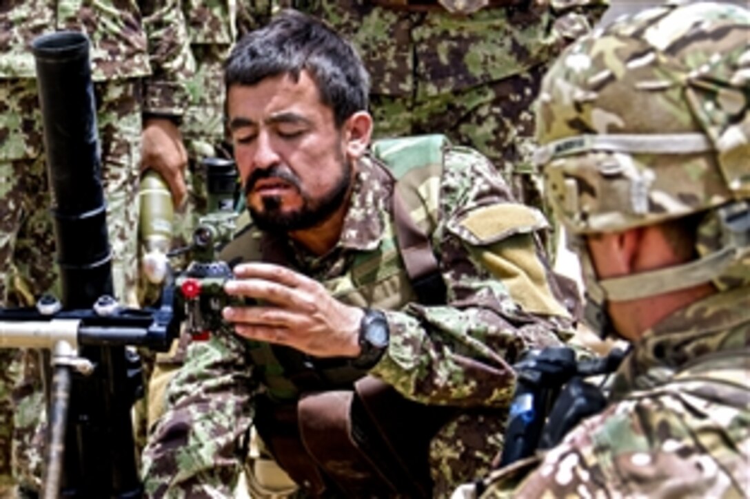 A U.S. soldier, right, observes as an Afghan soldier makes proper adjustments before loading a round in a 60mm mortar system in Afghanistan’s Ghazni province, July 7, 2013.