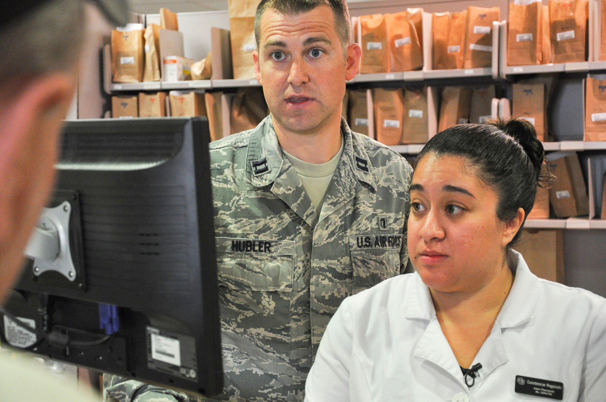 Capt. (Dr.) Sam Hubler, 460th Medical Group pharmacy operations officer, left, and Constencse Regalado, Buckley’s first University of Colorado pharmacy intern, assist an elderly customer with his medication July 1, 2013, at the pharmacy on Buckley Air Force Base, Colo. The internship program pairs students with highly trained military doctors. (U.S. Air Force photo by Staff Sgt. Nicholas Rau/Released)