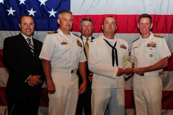 Rear Adm. Richard Breckenridge (right), Undersea Warfare Division director, and Cmdr. Charles Phillip, Navy Munitions Command Unit Charleston commanding officer, presents Petty Officer 2nd Class Noah Kalemkiewicz the Enlisted Active-Duty Person of the Year,  during the “Salute the Military” ceremony June 27, 2013, at the North Charleston Performing Arts Center, North Charleston, S.C. (From left to right) Jon Rudy of General Dynamics Land Systems Force Protection, the Title Sponsor, and Mr. Stuart Whiteside, Charleston Metro Chamber Chairman of the Board, also are  pictured here. Kalemkiweicz volunteered nearly 350 hours of his time to community service. Kalemkiewicz, a mineman, is currently the work center supervisor for the quality assurance department at the Navy Munitions Command at JB Charleston – Weapons Station. (U.S. Air Force photo/Staff Sgt. Rasheen Douglas)